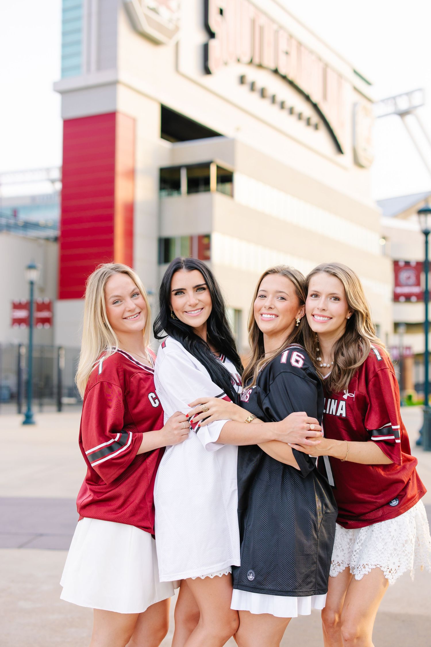 Four friends hugging in South Carolina Gamecocks jerseys outside Williams-Brice Stadium.