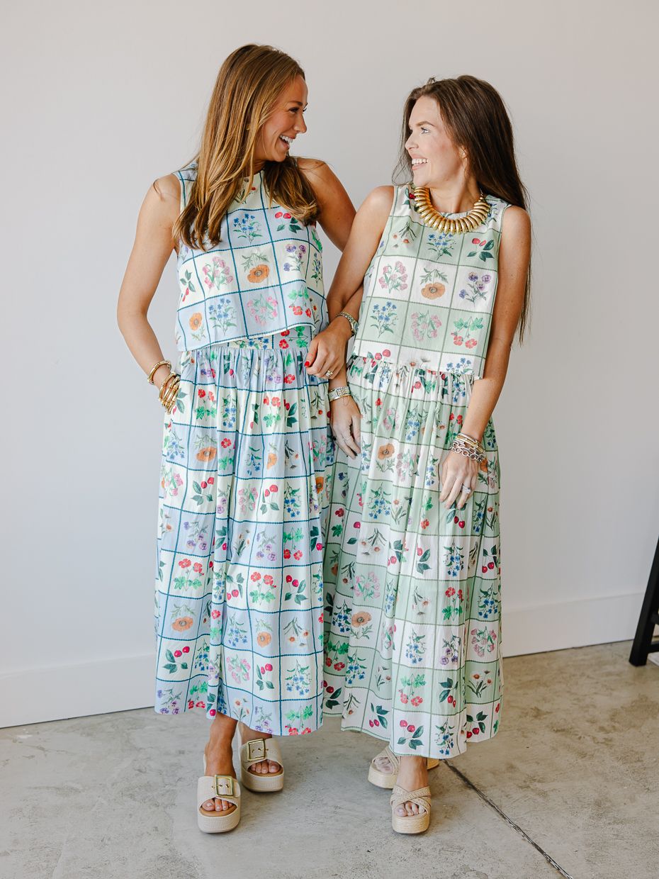 Two women in floral botanical print sleeveless midi dresses smiling together indoors.