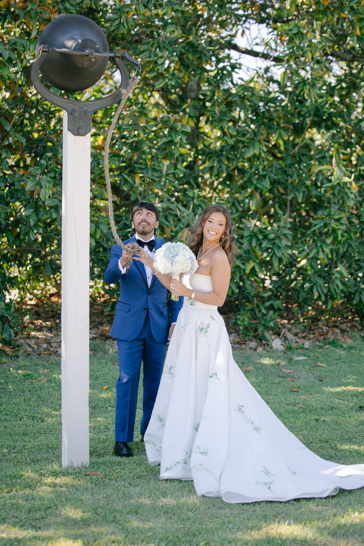 Bride and groom laughing together outdoors near a vintage lamp post, bride holding white bouquet in embroidered wedding gown.