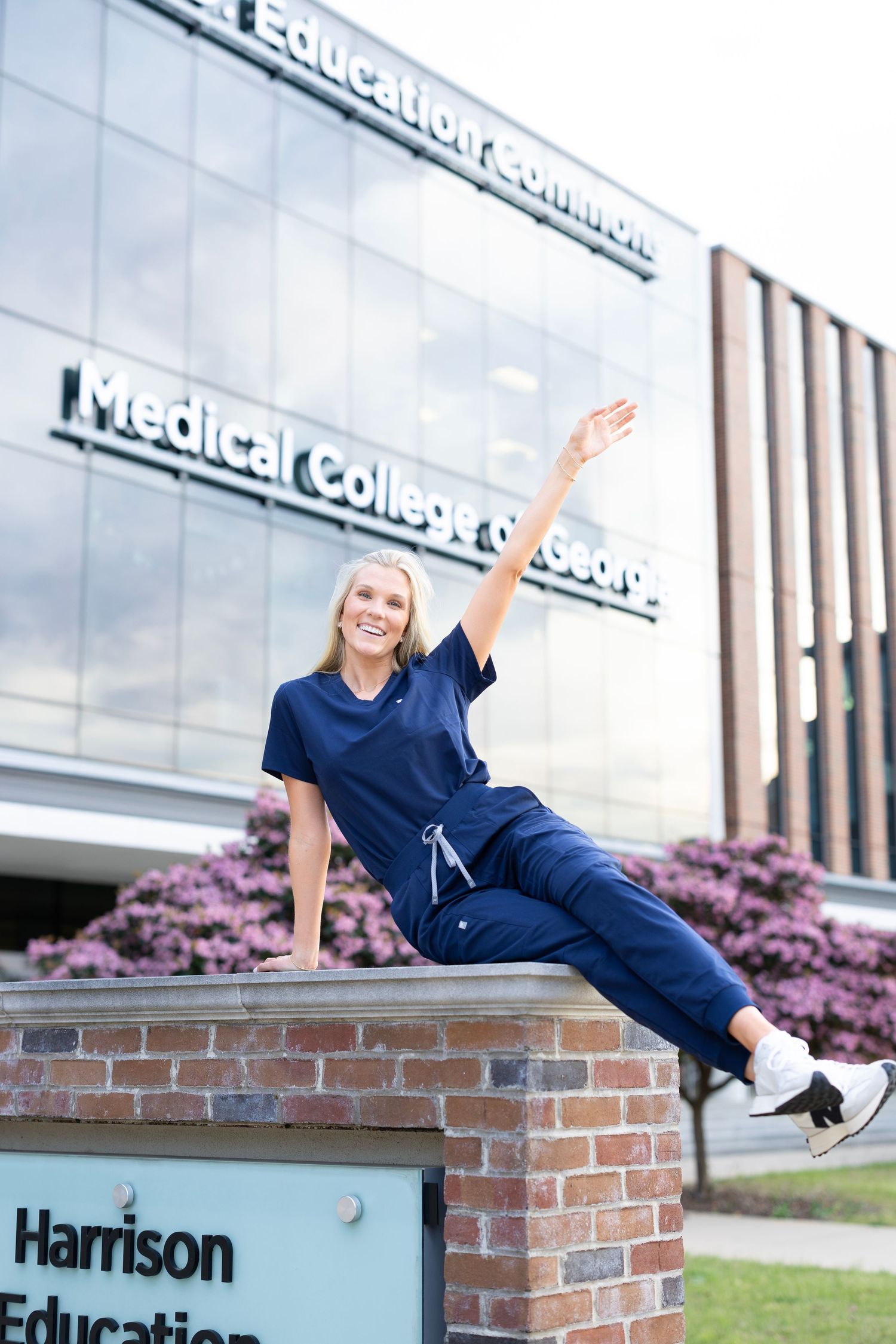 Nursing student in navy scrubs sits on Medical College of Georgia Harrison Education Commons sign.