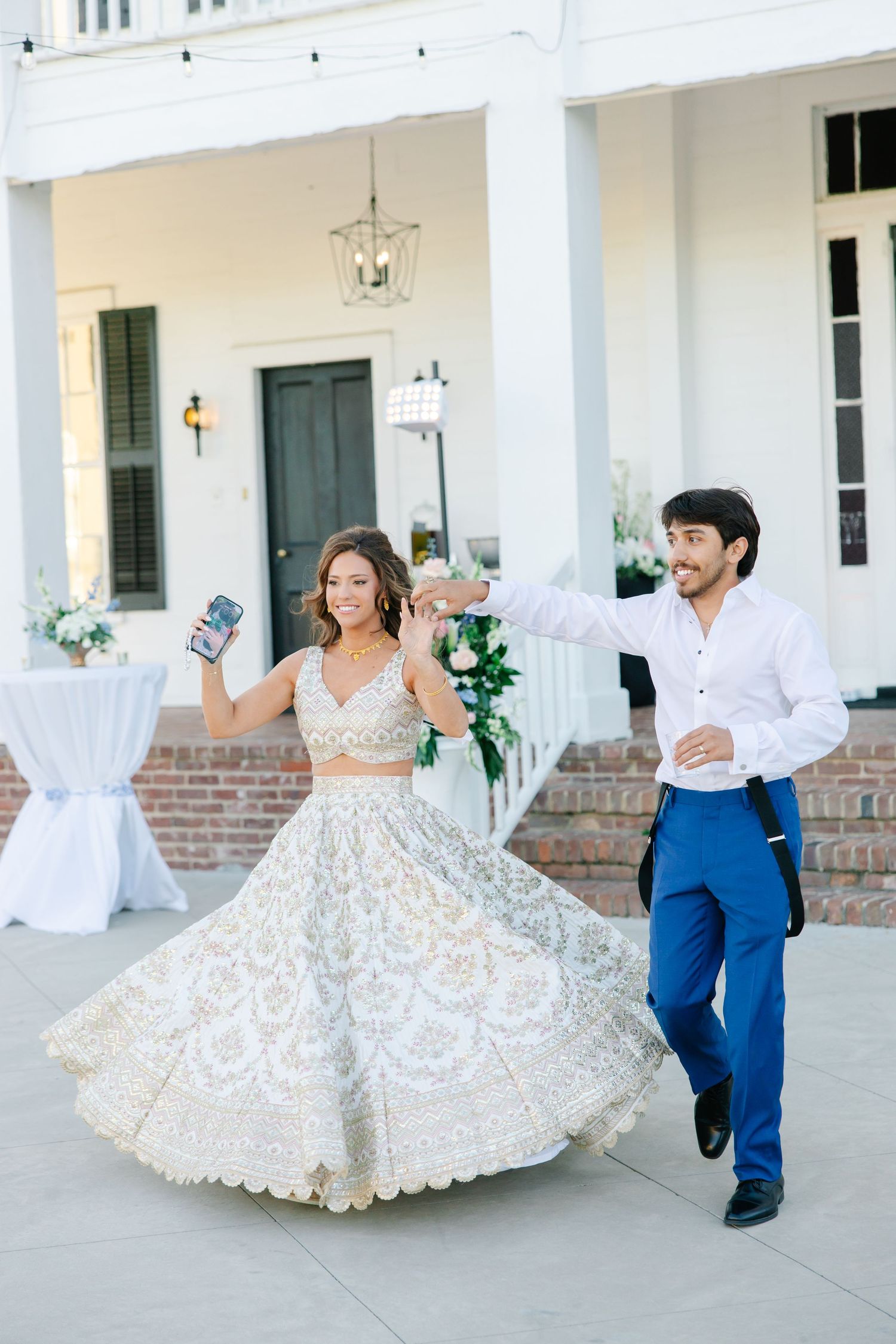 Bride in embroidered lehenga twirling with groom in blue suit during wedding reception entrance.