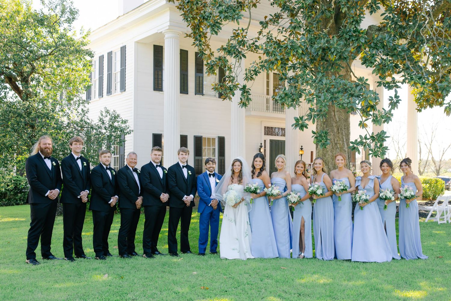 Full wedding party posing outside historic venue with bridesmaids in blue gowns.