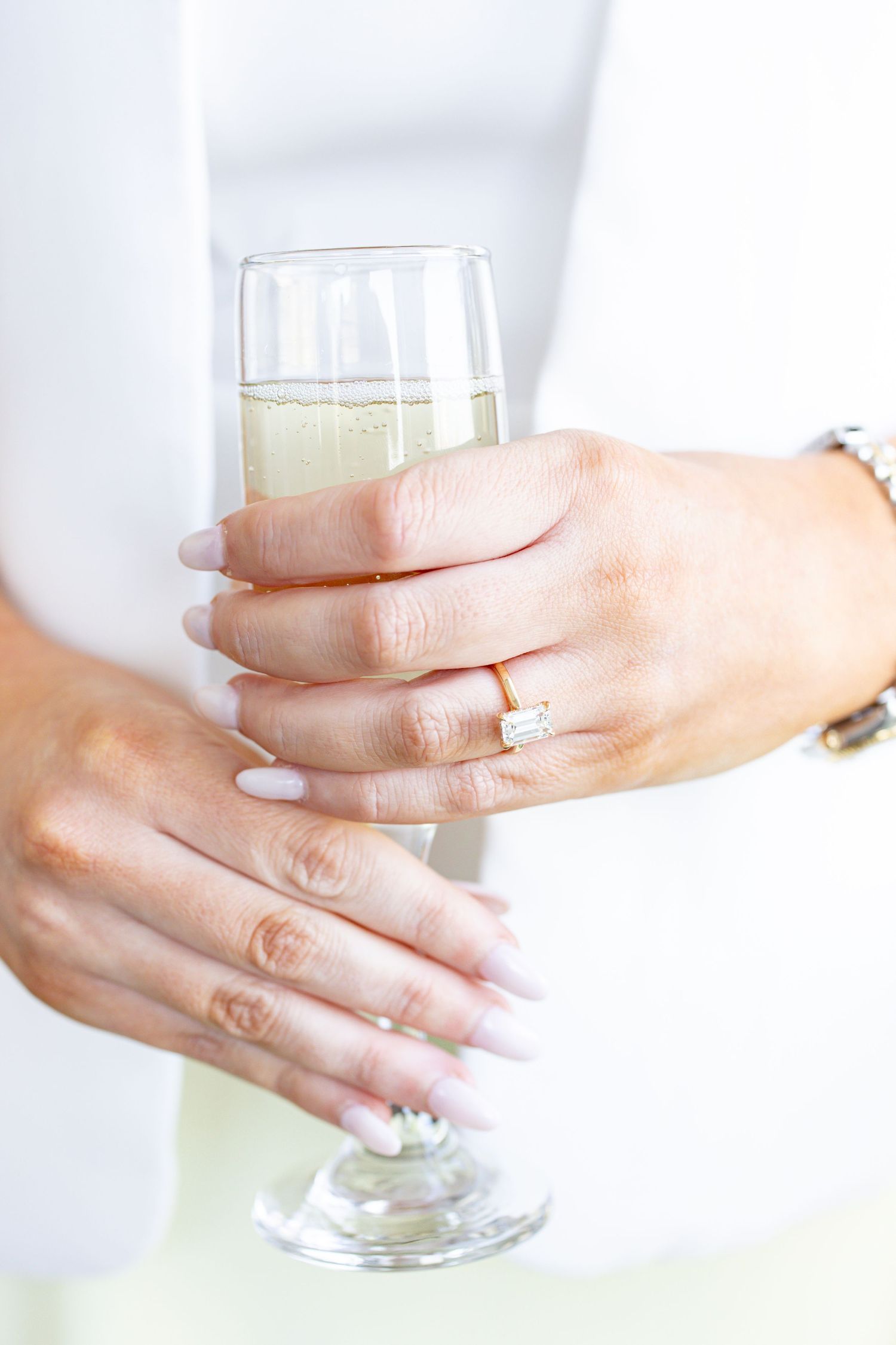 Close-up of woman's hands holding a champagne flute wearing a diamond engagement ring.