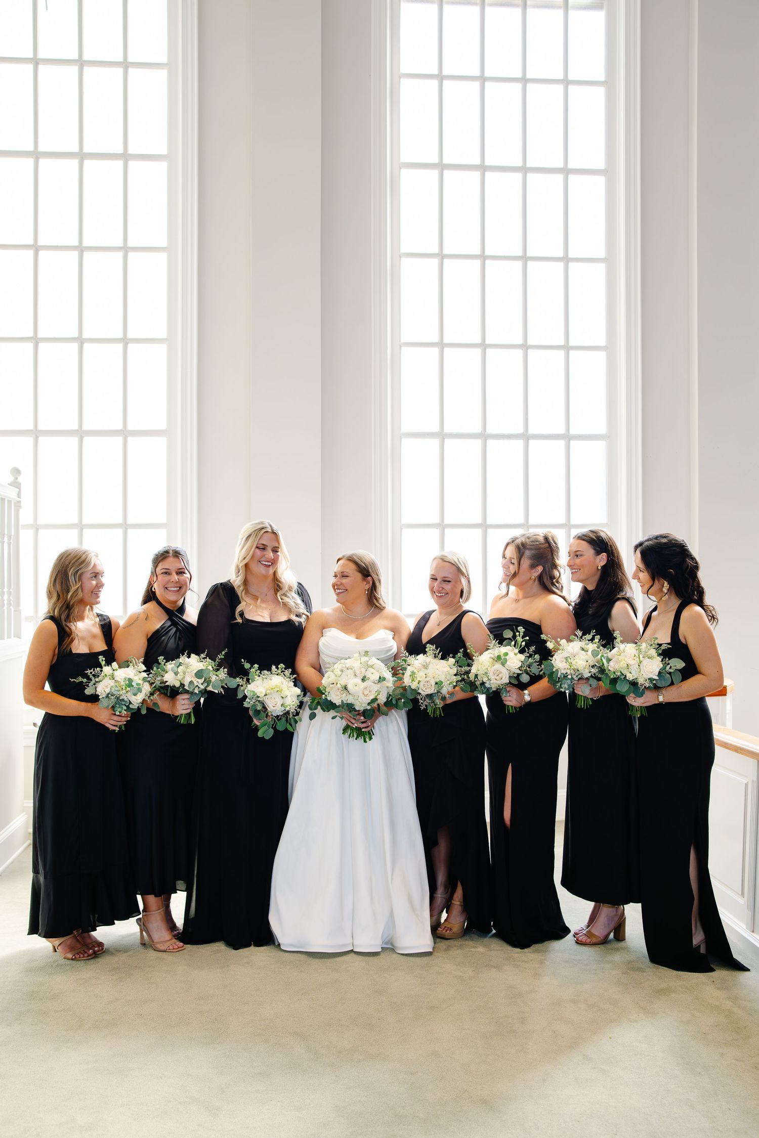 Bride in white strapless gown surrounded by bridesmaids in black dresses holding white bouquets.