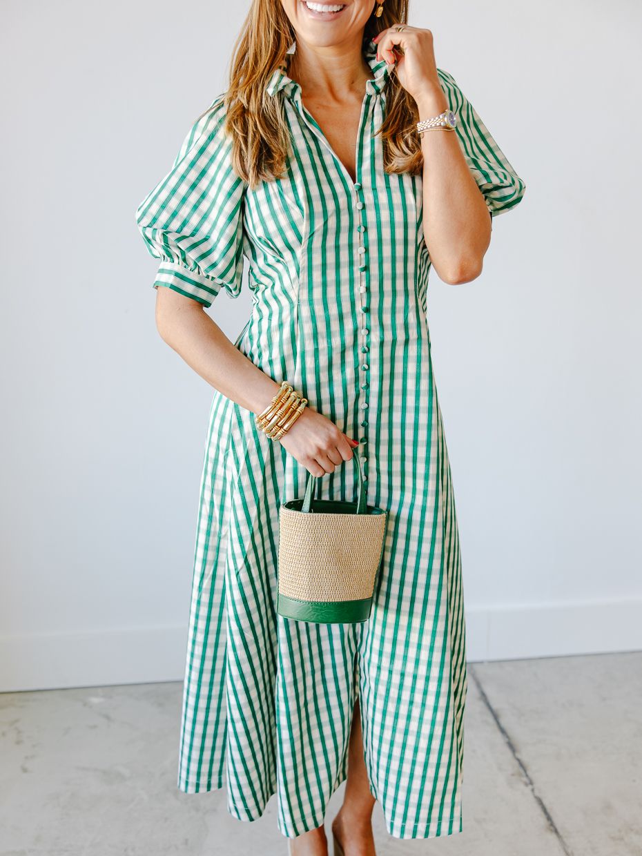 Woman in a green gingham midi shirtdress with puff sleeves, holding a woven bucket bag with green trim.