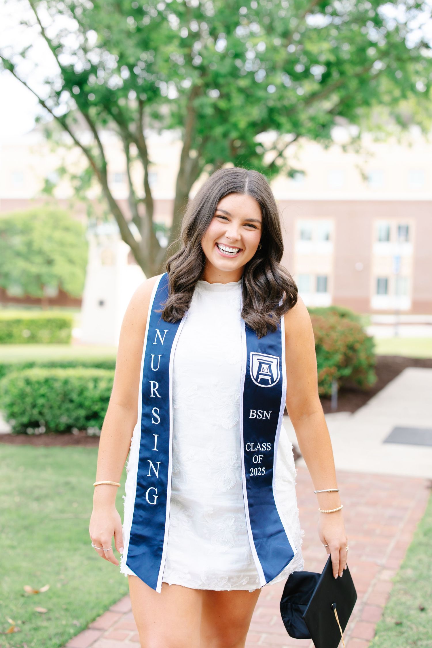 Nursing BSN Class of 2025 graduate smiling in navy stole holding cap on Augusta University campus.