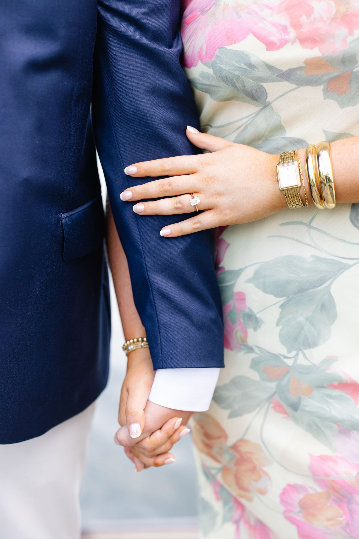 Close-up of woman showing diamond engagement ring while holding hands with man in navy suit.