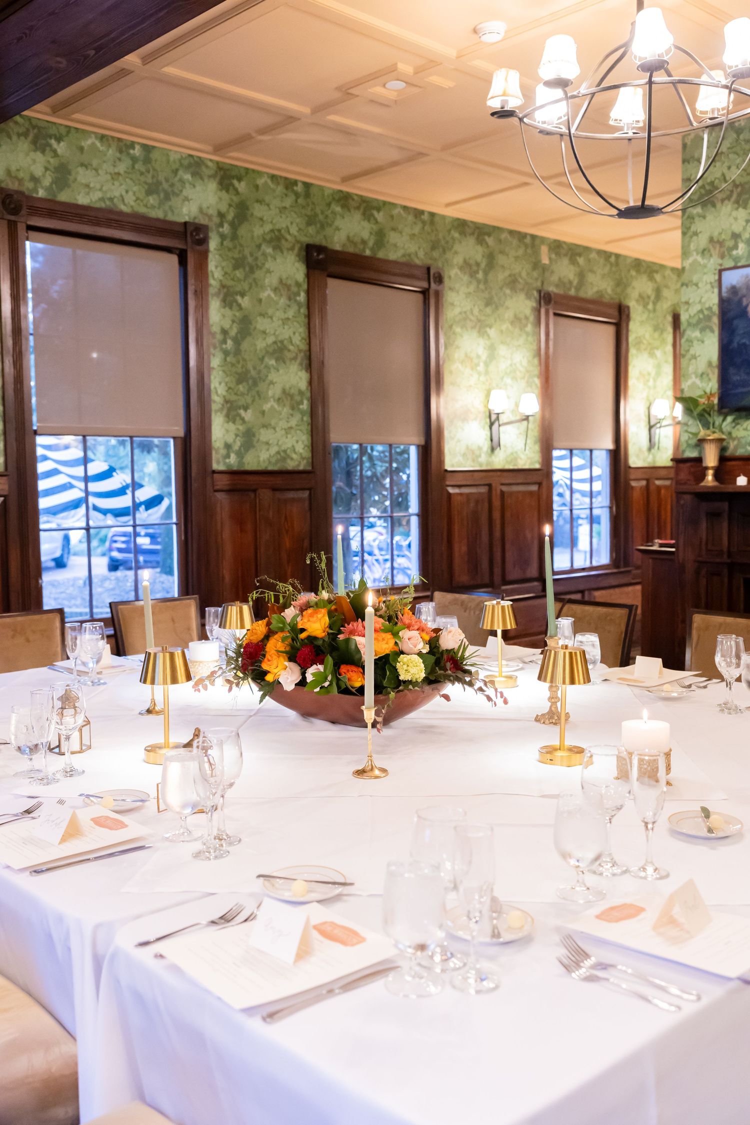 Formal dining room with green wallpaper, wood paneling, white tablecloths, and floral centerpieces for a special event.