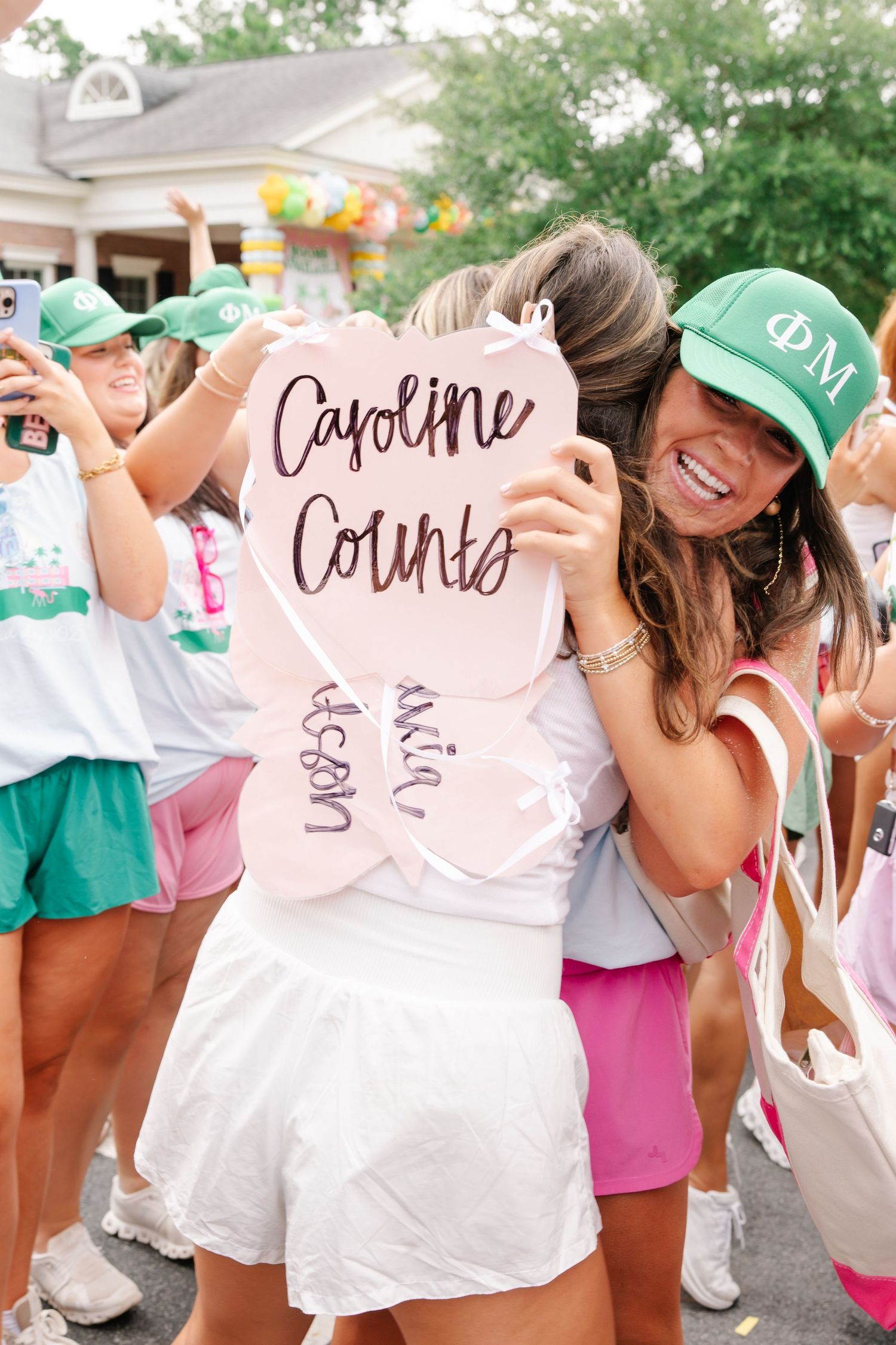Phi Mu sorority member holds pink bid day sign reading Caroline Counts while hugging a new member.
