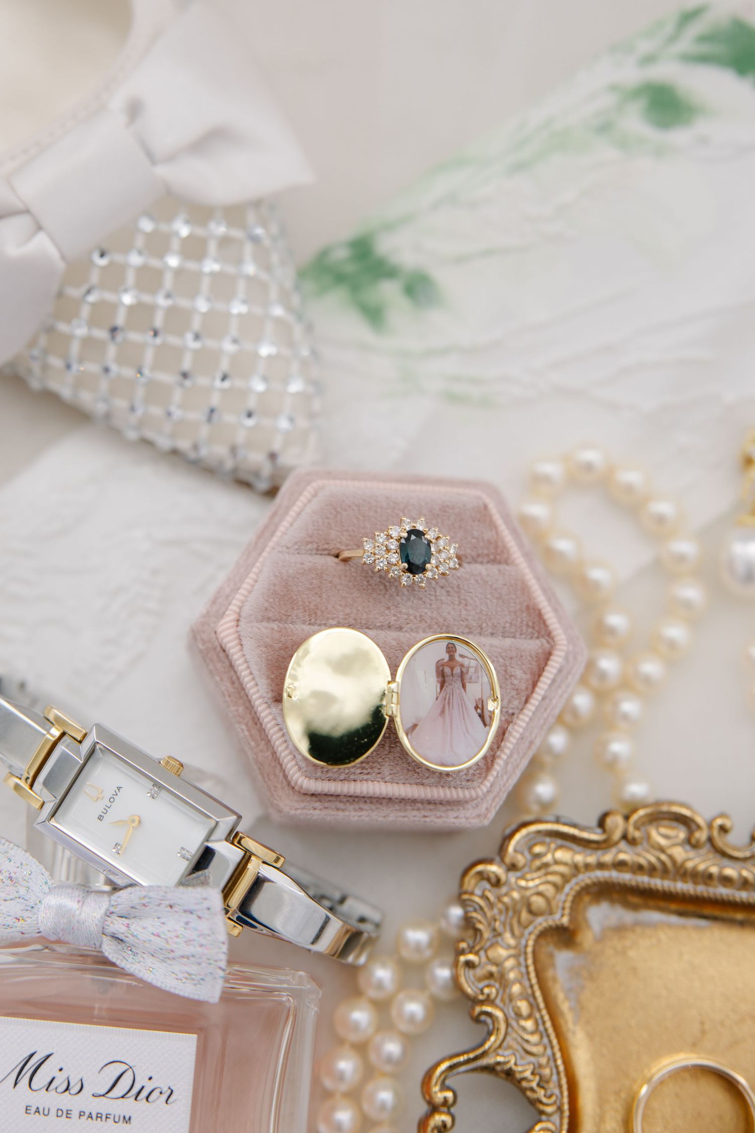 Gold locket and sapphire ring displayed in pink velvet box surrounded by pearls and Miss Dior perfume.