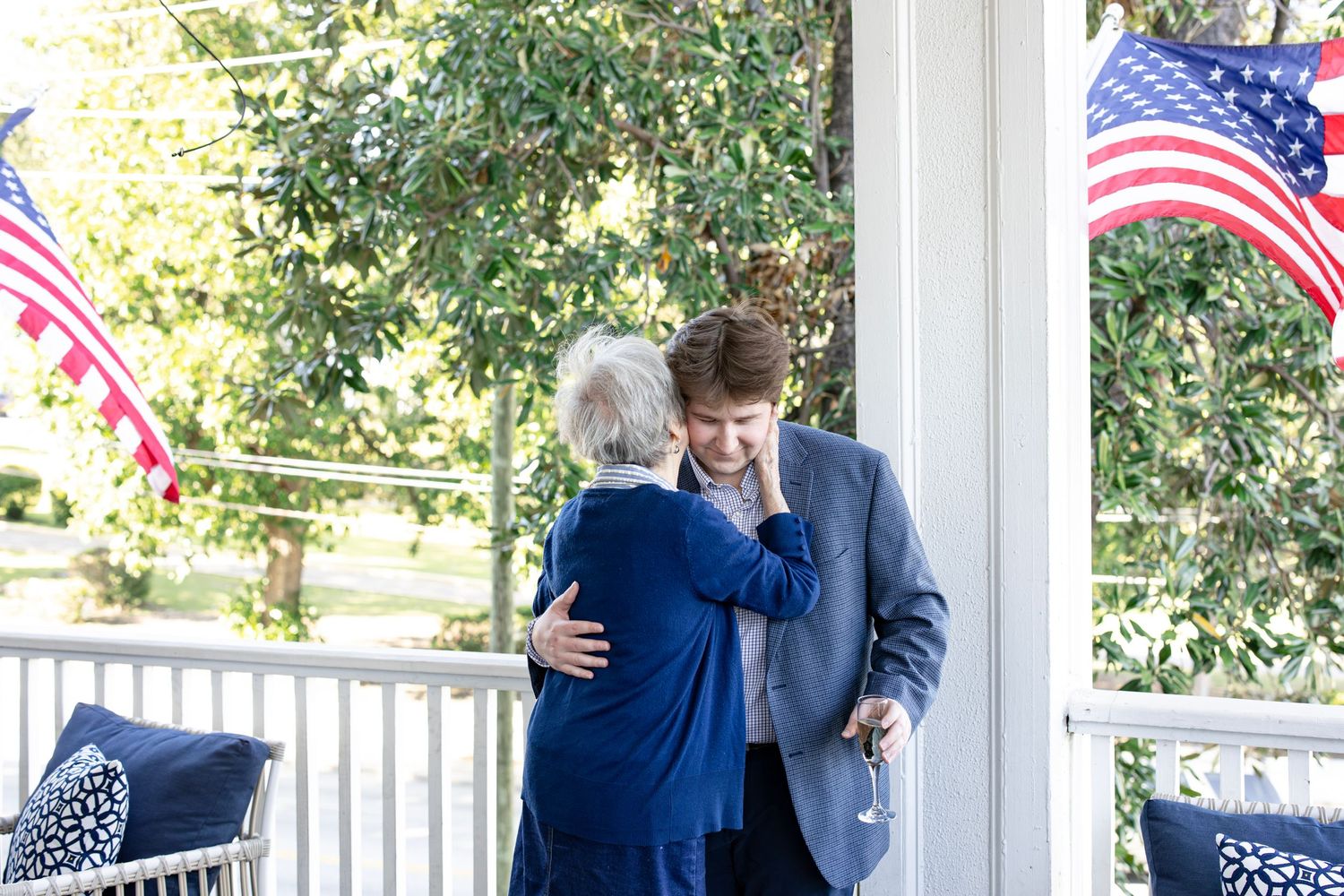 Two women sharing a warm embrace on a porch decorated with American flags.