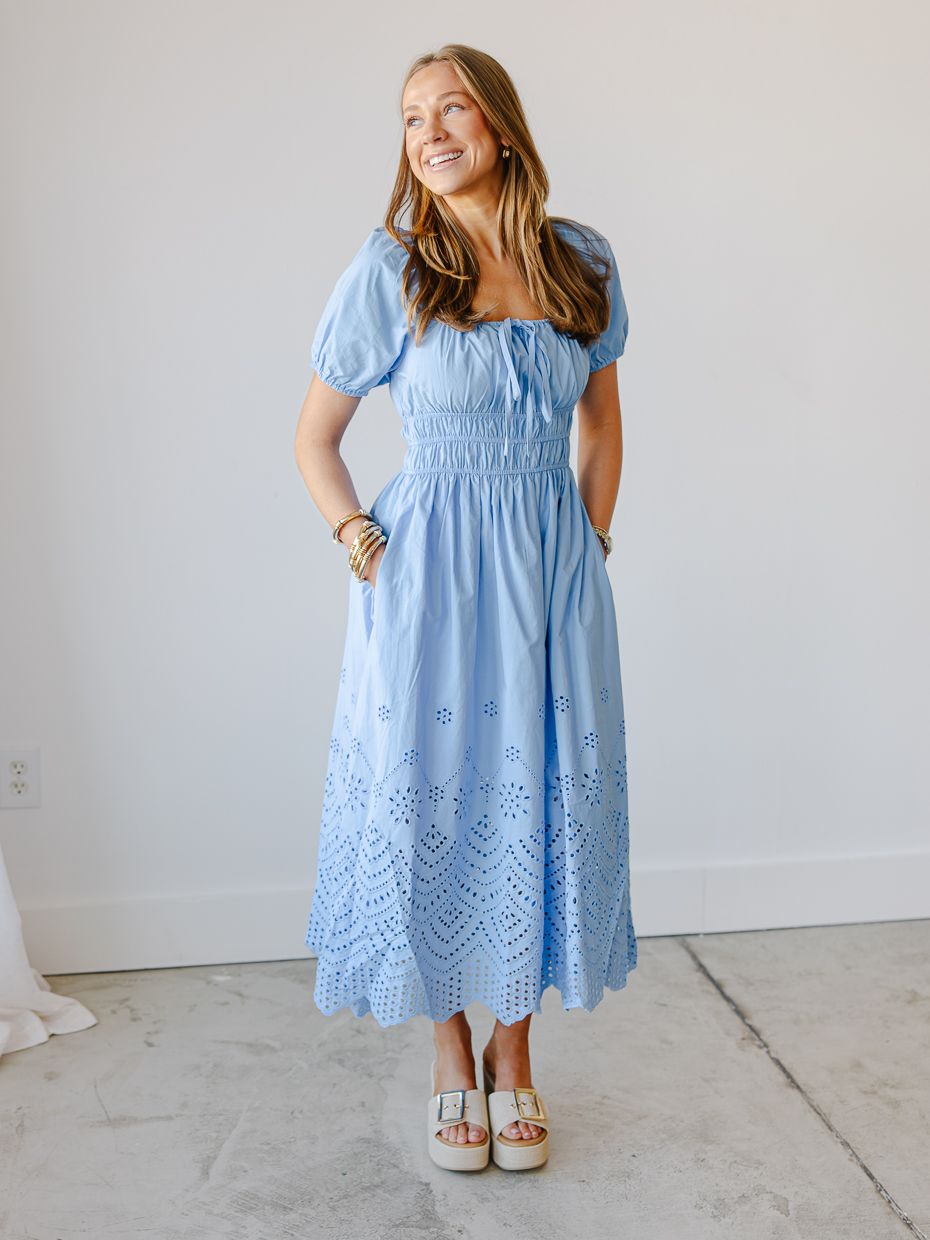 Woman in a blue eyelet midi dress with smocked bodice and puff sleeves paired with white platform sandals.