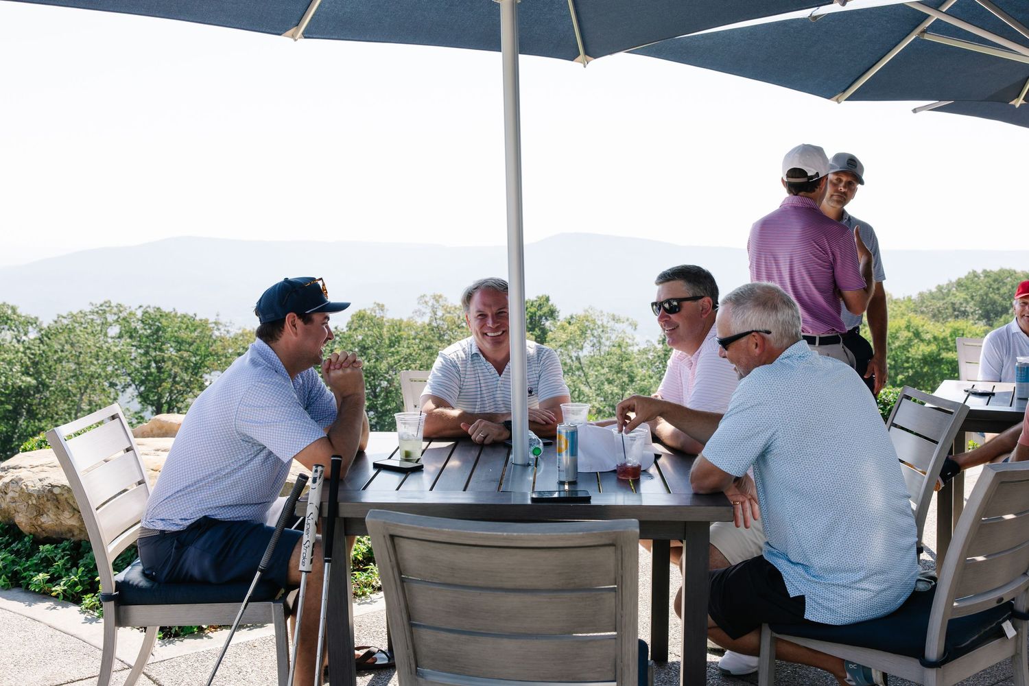 Group of golfers socializing at an outdoor patio table with mountain views in the background.