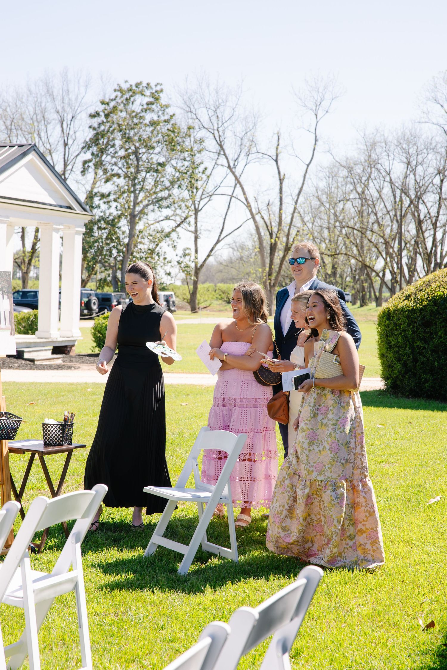 Wedding guests in formal attire socializing on green lawn at outdoor garden ceremony.
