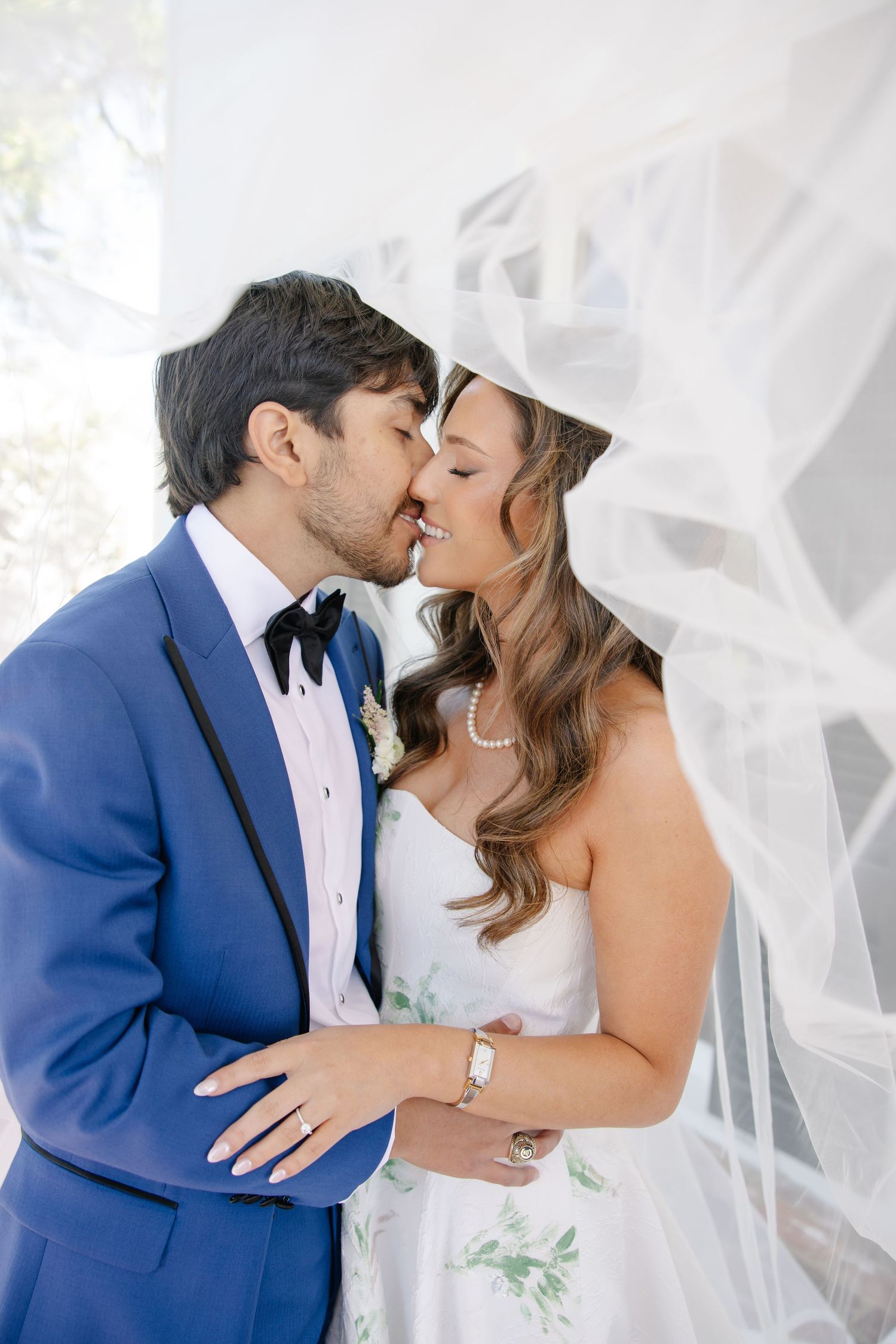 Bride and groom sharing a romantic kiss under a flowing white veil on their wedding day.