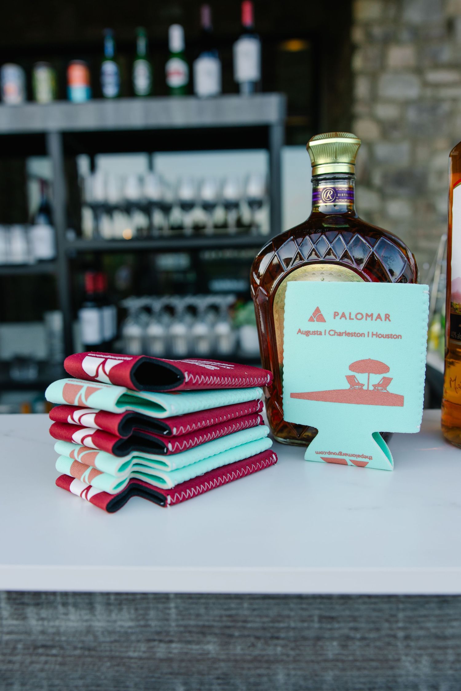 Palomar branded merchandise display with colorful towels and a whiskey bottle on a white counter.