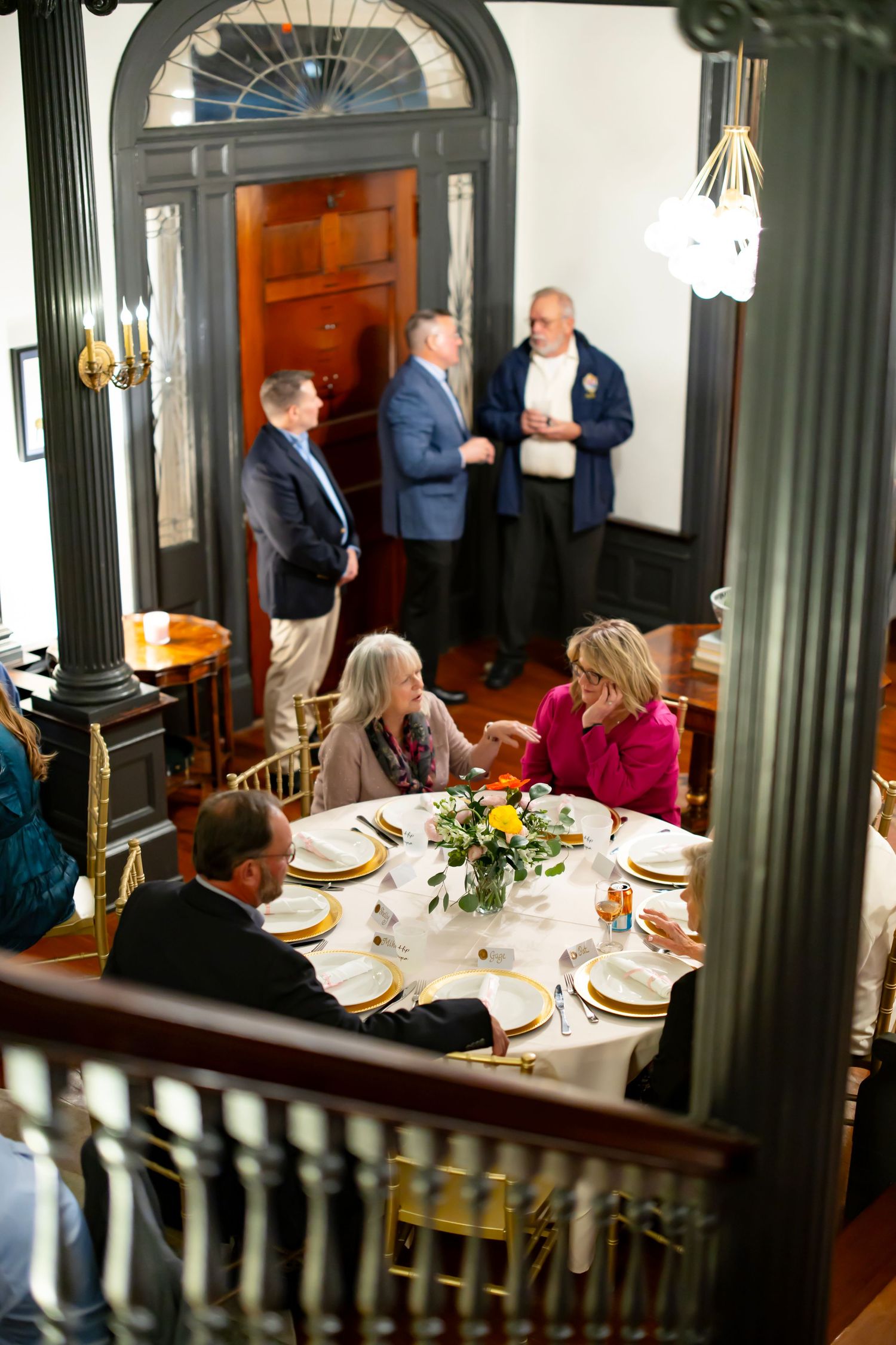 Overhead view of wedding reception guests socializing at elegantly set round table in historic venue.