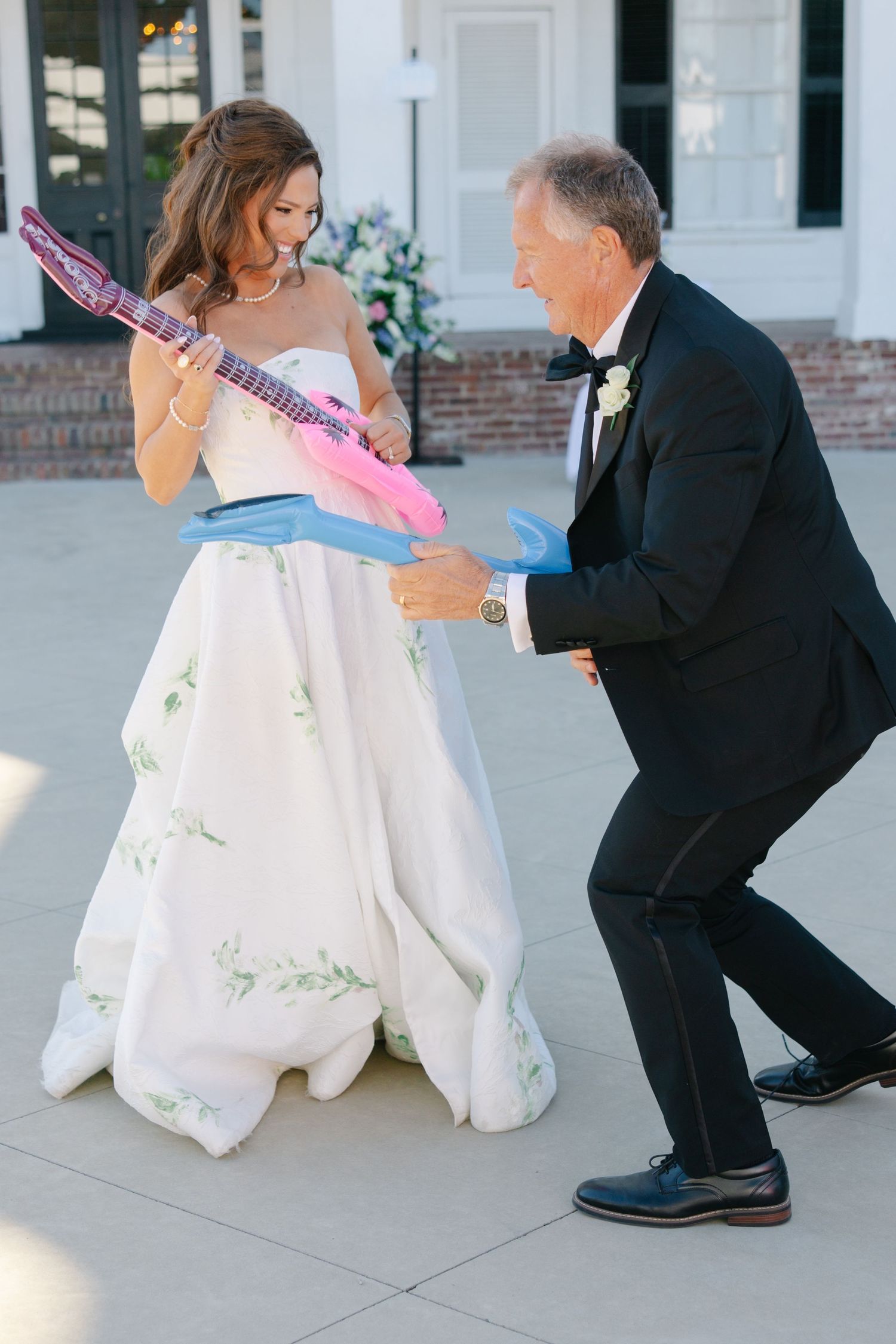 Bride and father playfully air guitar with inflatable instruments during wedding reception dance.