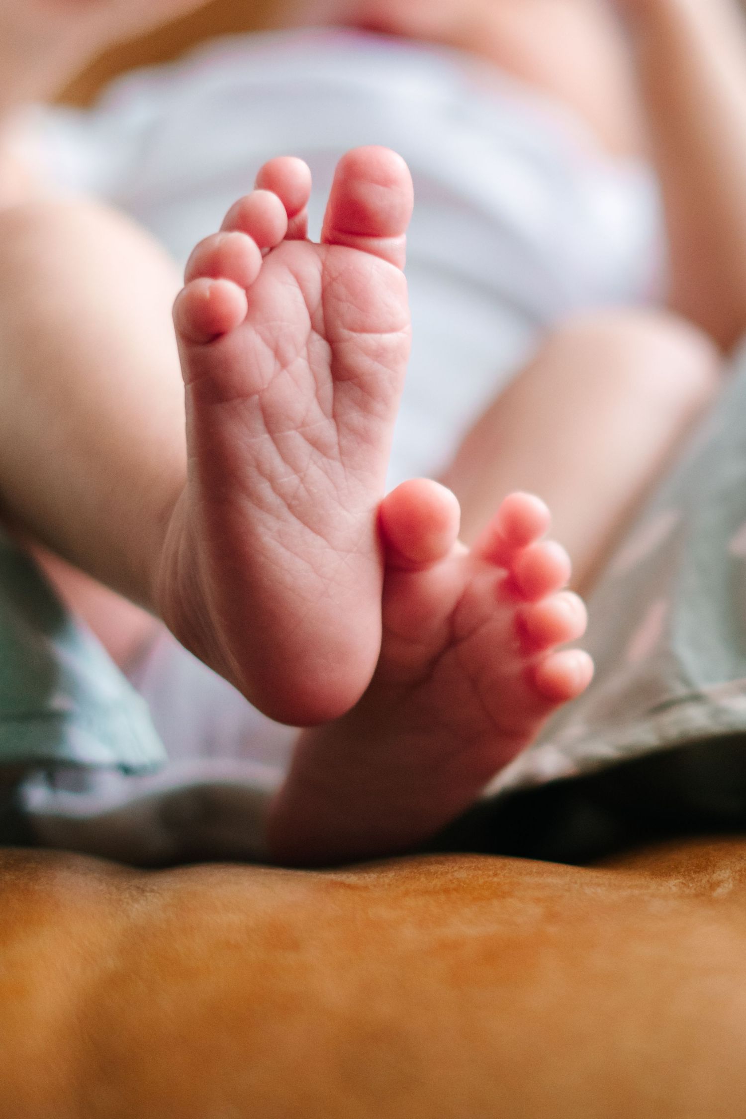 Close-up of tiny newborn baby feet with small toes resting on a soft brown surface.