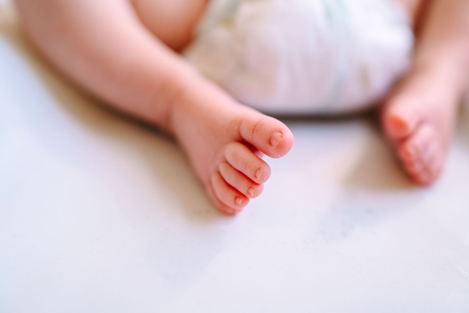Close-up of tiny newborn baby feet resting on a soft white blanket, showcasing delicate toes and smooth skin.