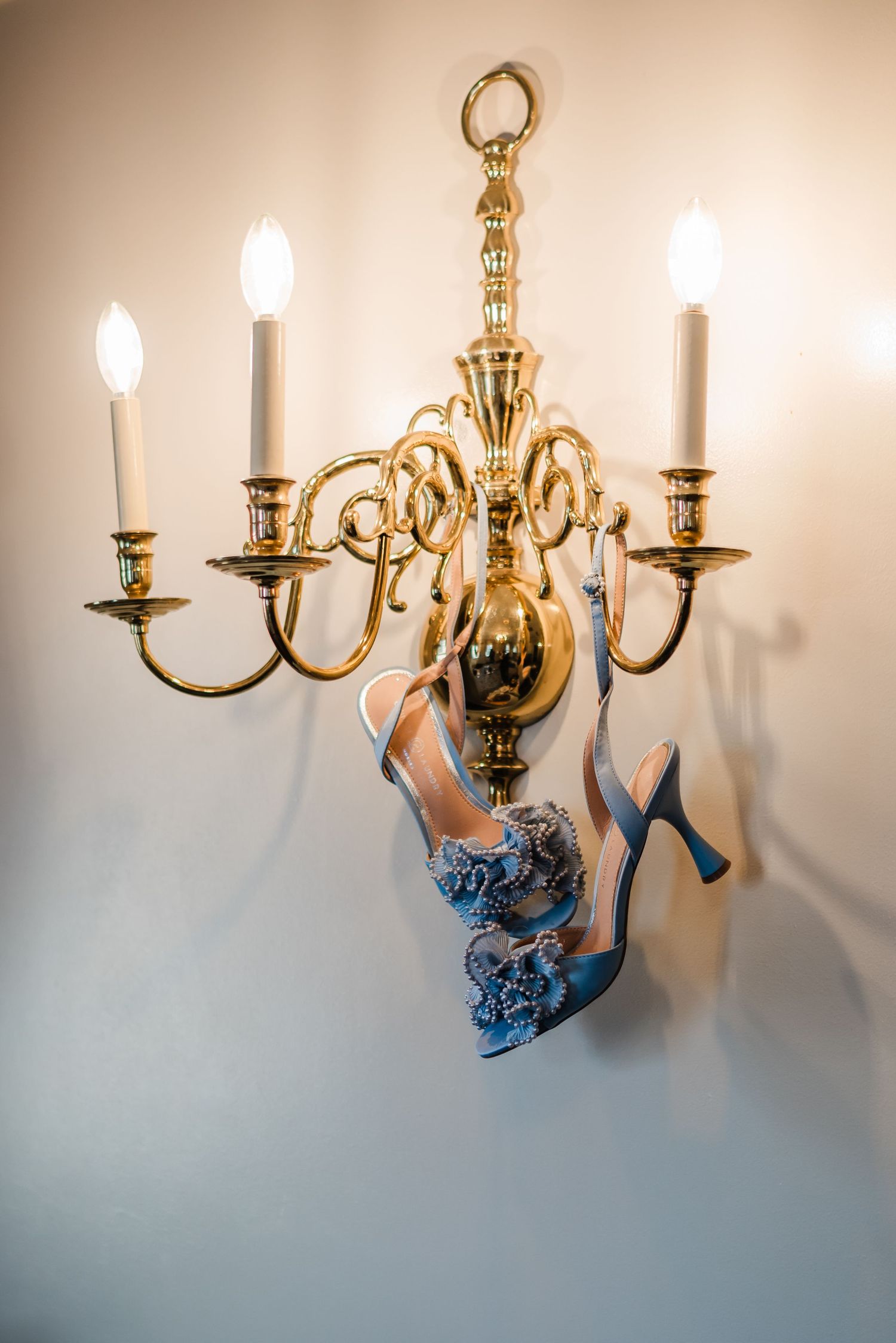 Blue floral heeled wedding shoes hanging from a gold candelabra wall sconce with lit candles Hotel DuPont wedding Philadelphia photographer