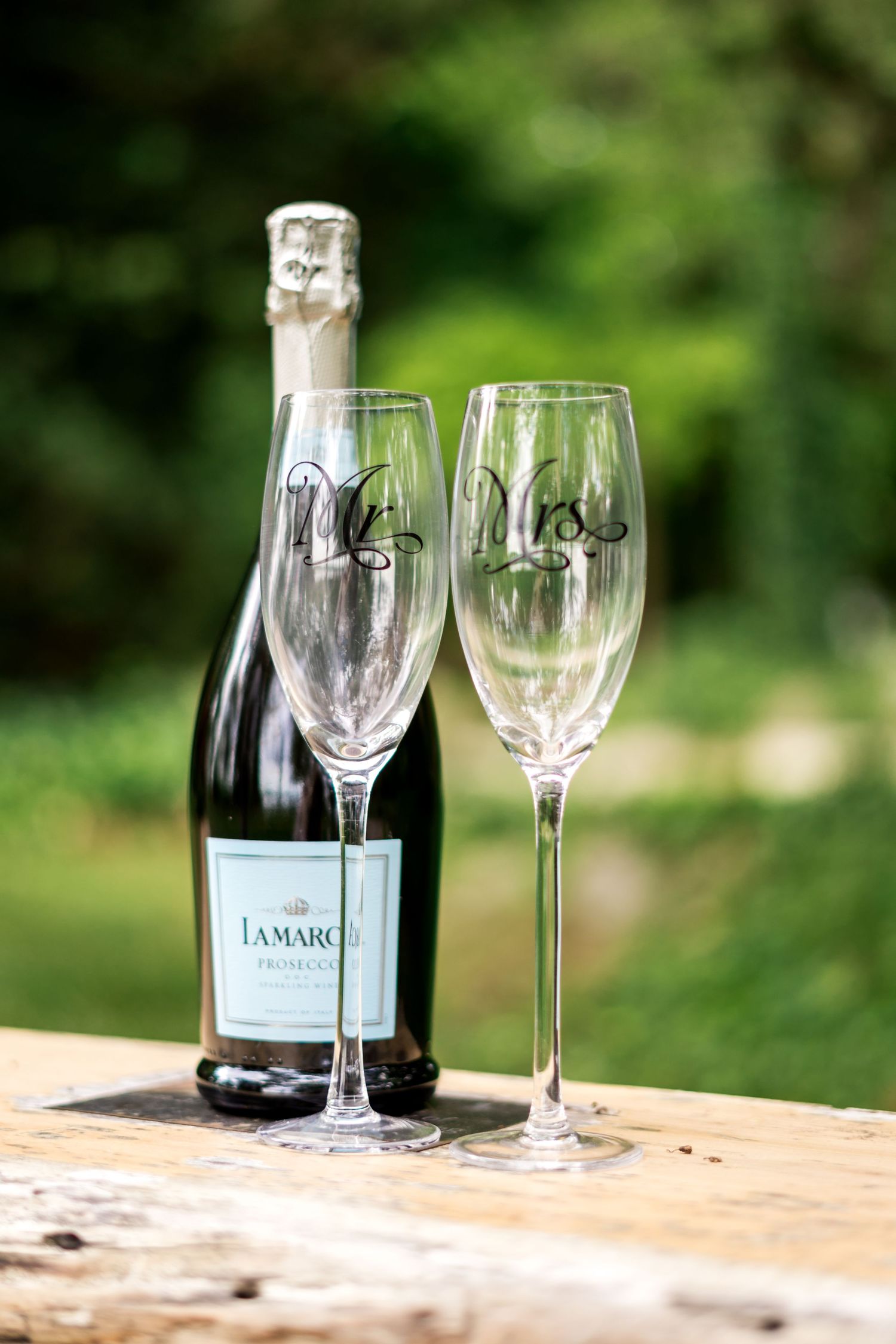 La Marca Prosecco bottle with Mr. and Mrs. champagne flutes on rustic wood surface, perfect for weddings.
