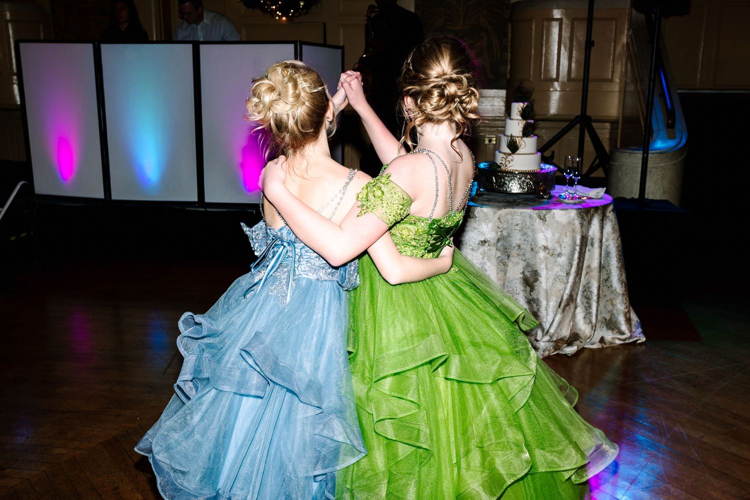 Hotel DuPont wedding Philadelphia Two girls in blue and green ball gowns dancing together at a formal event with decorative lighting.