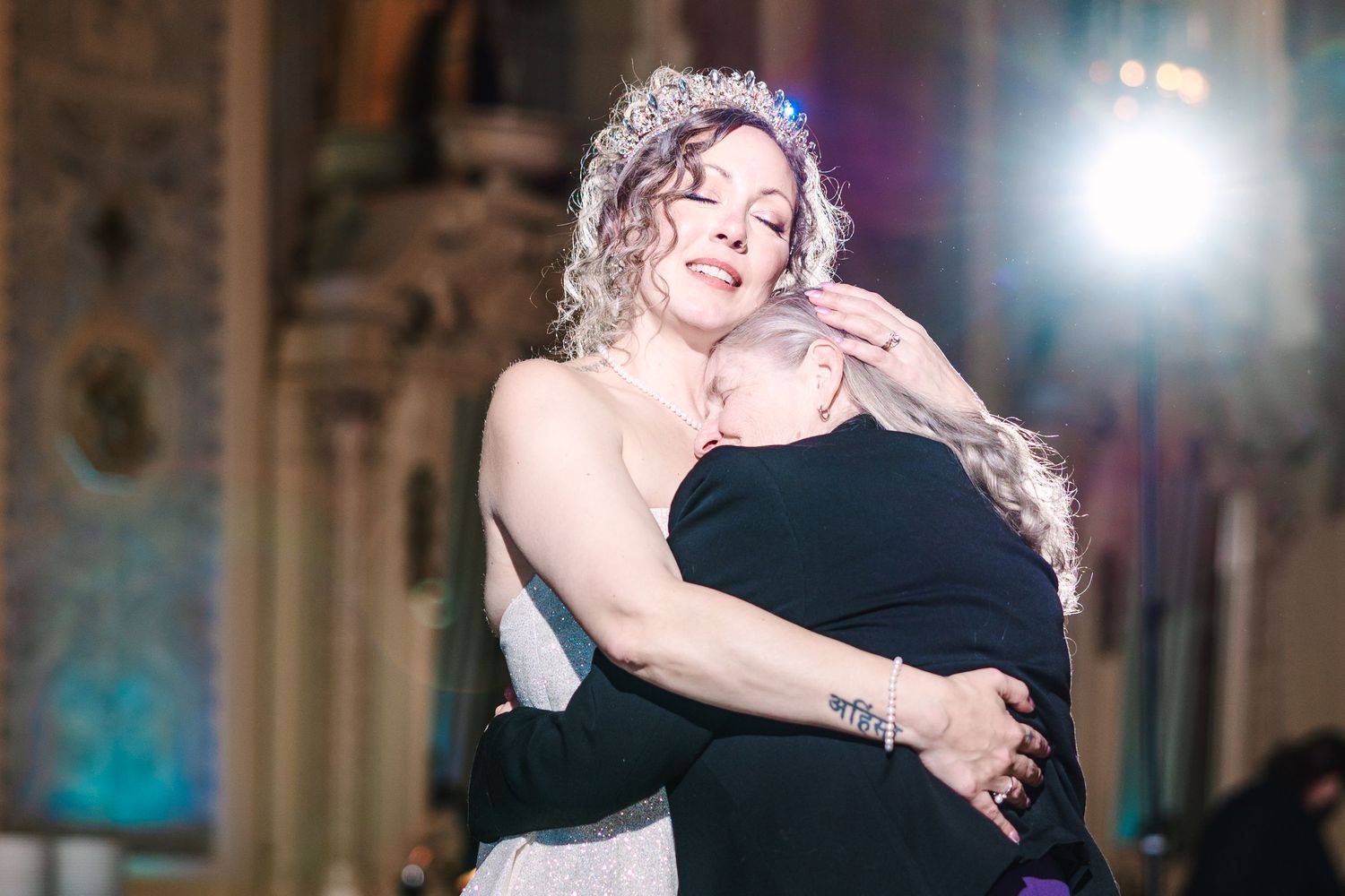 Hotel DuPont wedding Philadelphia photographer Two women share a warm embrace at an elegant venue, one wearing a bridal gown and tiara.