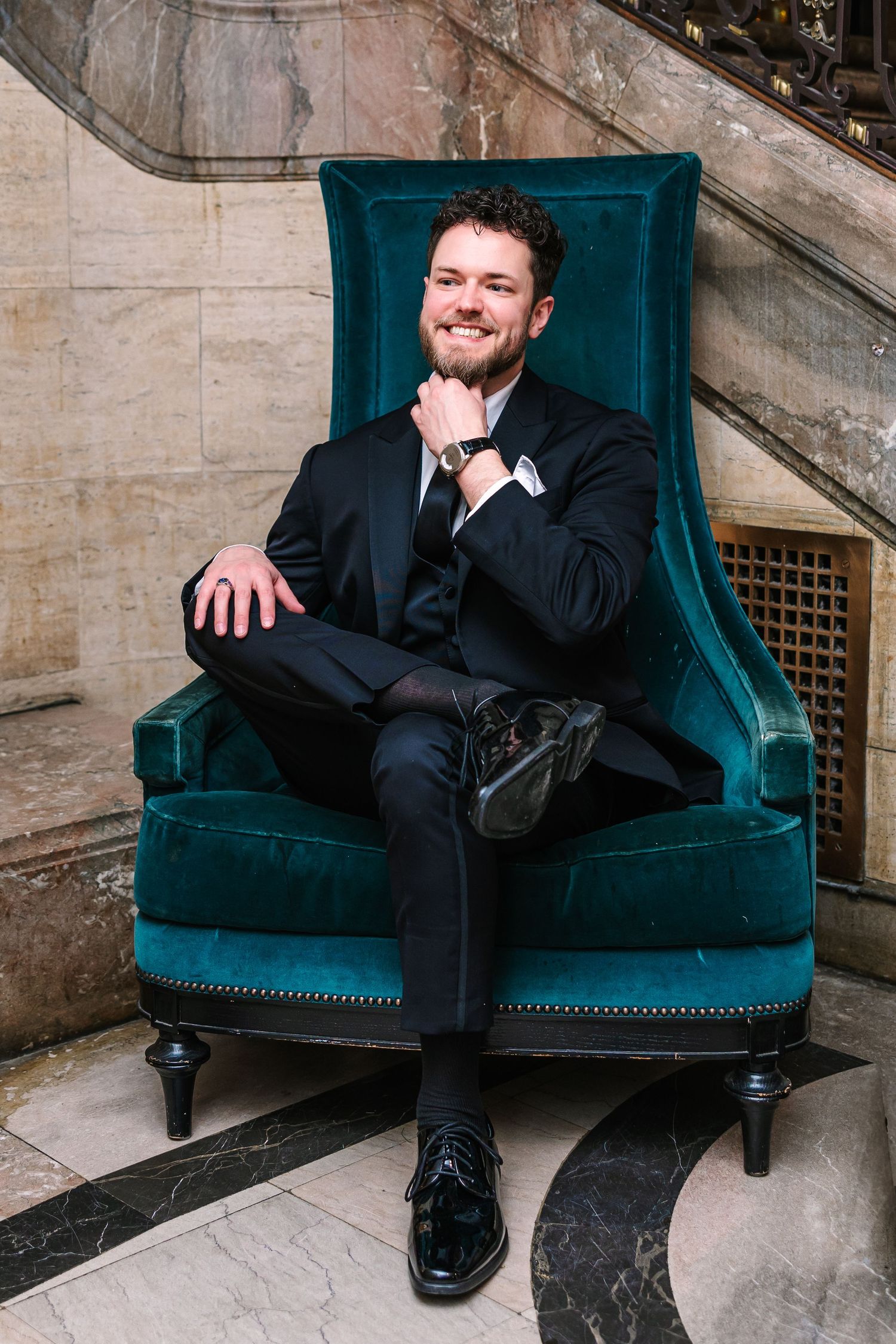 Hotel DuPont wedding Philadelphia photographer Groom in black tuxedo sitting in teal velvet chair at Hotel Du Pont.