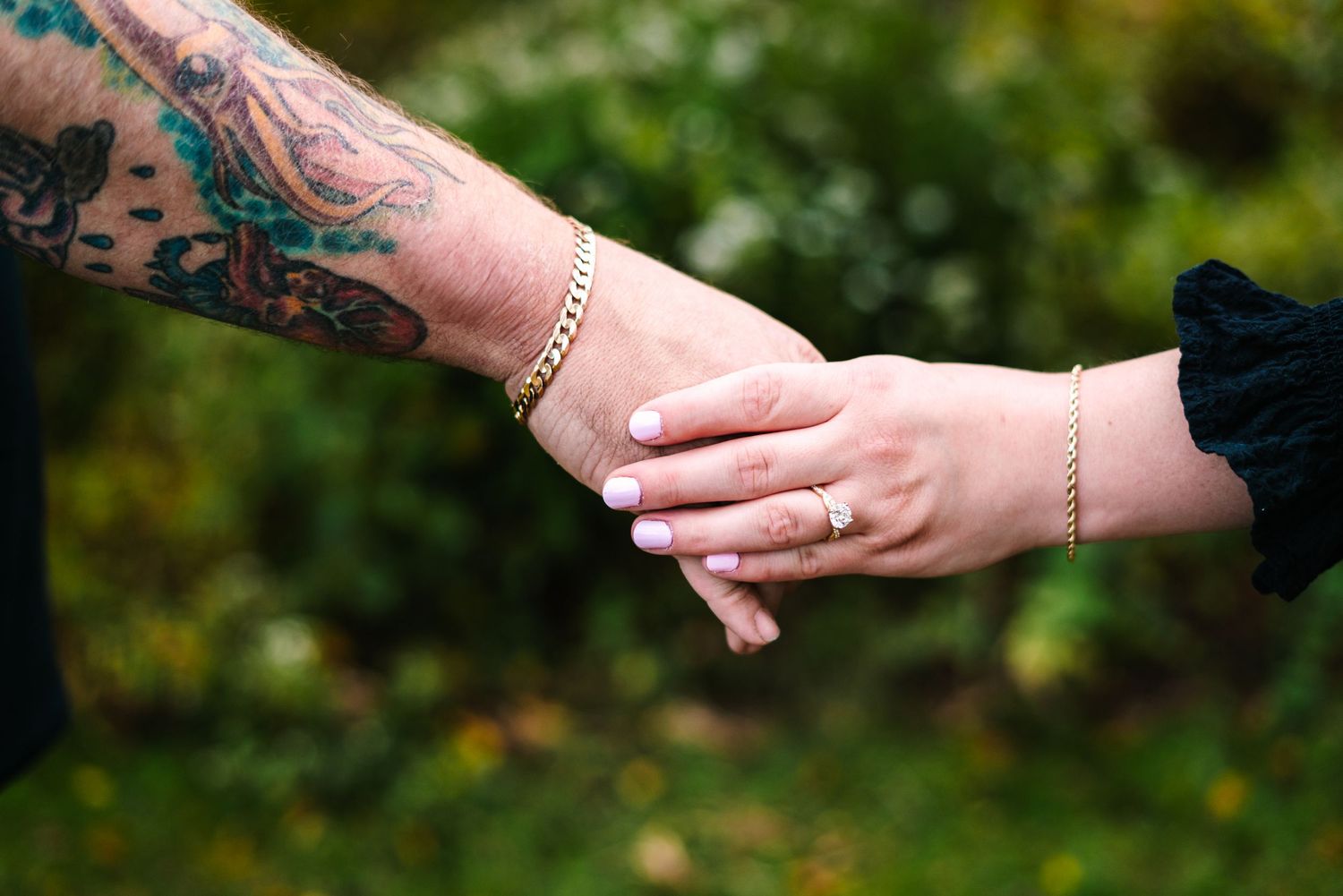 Tattooed arm and delicate hand with gold ring and bracelet holding hands outdoors philadelphia wedding photographer