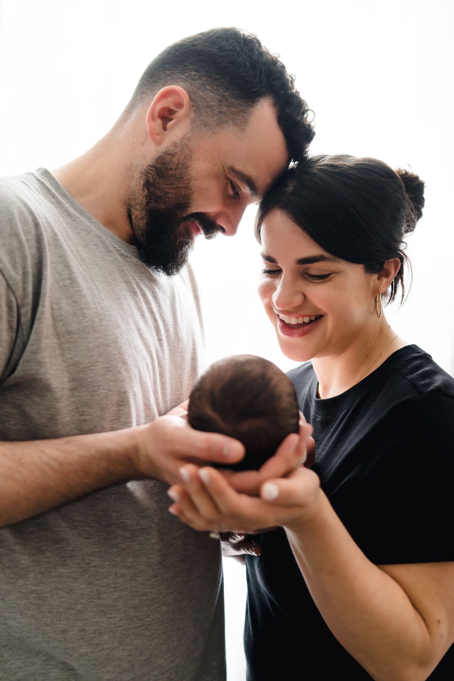 Happy couple smiling while gently cradling their newborn baby in their hands together.
