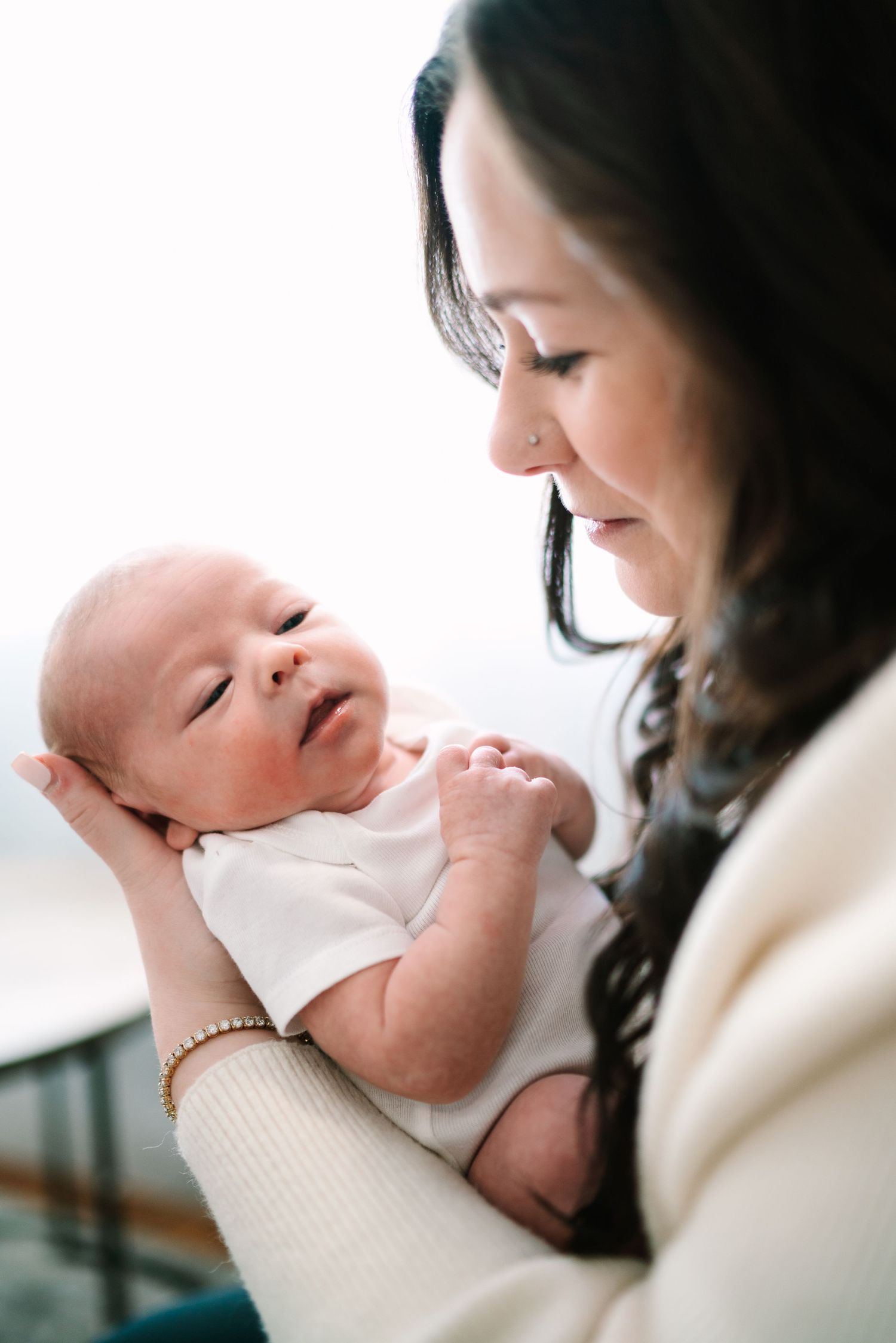 A mother tenderly gazes at her newborn baby dressed in white, cradling the infant in her arms.