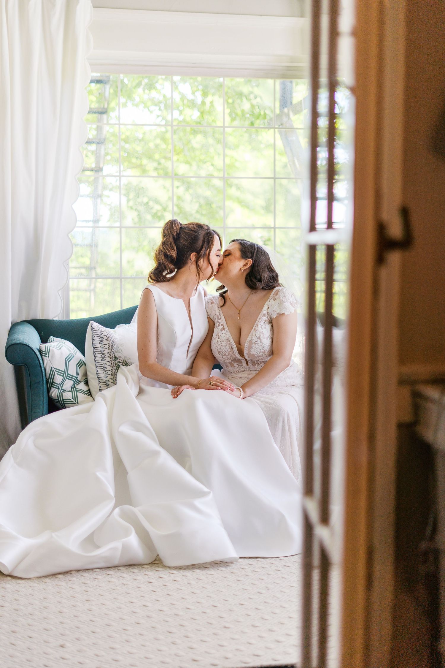 Fernbrook farms Philly wedding Two brides in white wedding gowns share a romantic moment seated by a sunlit window on their wedding day.