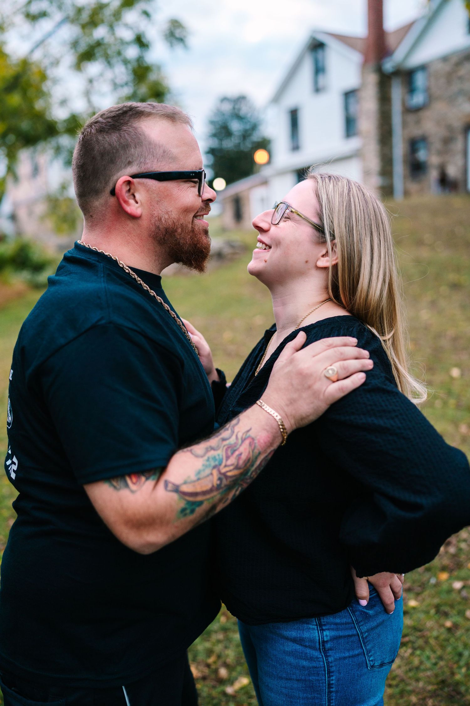 philadelphia wedding photographer Couple smiling and embracing outdoors, man with tattoos and glasses, woman in black top and jeans.