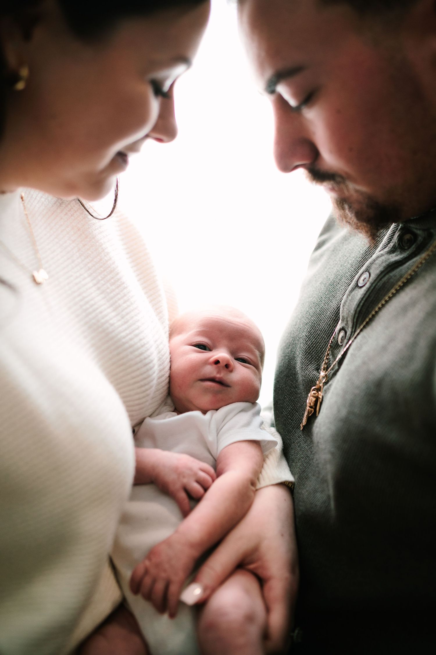 New parents tenderly hold their newborn baby, bowing heads together in an intimate family portrait.