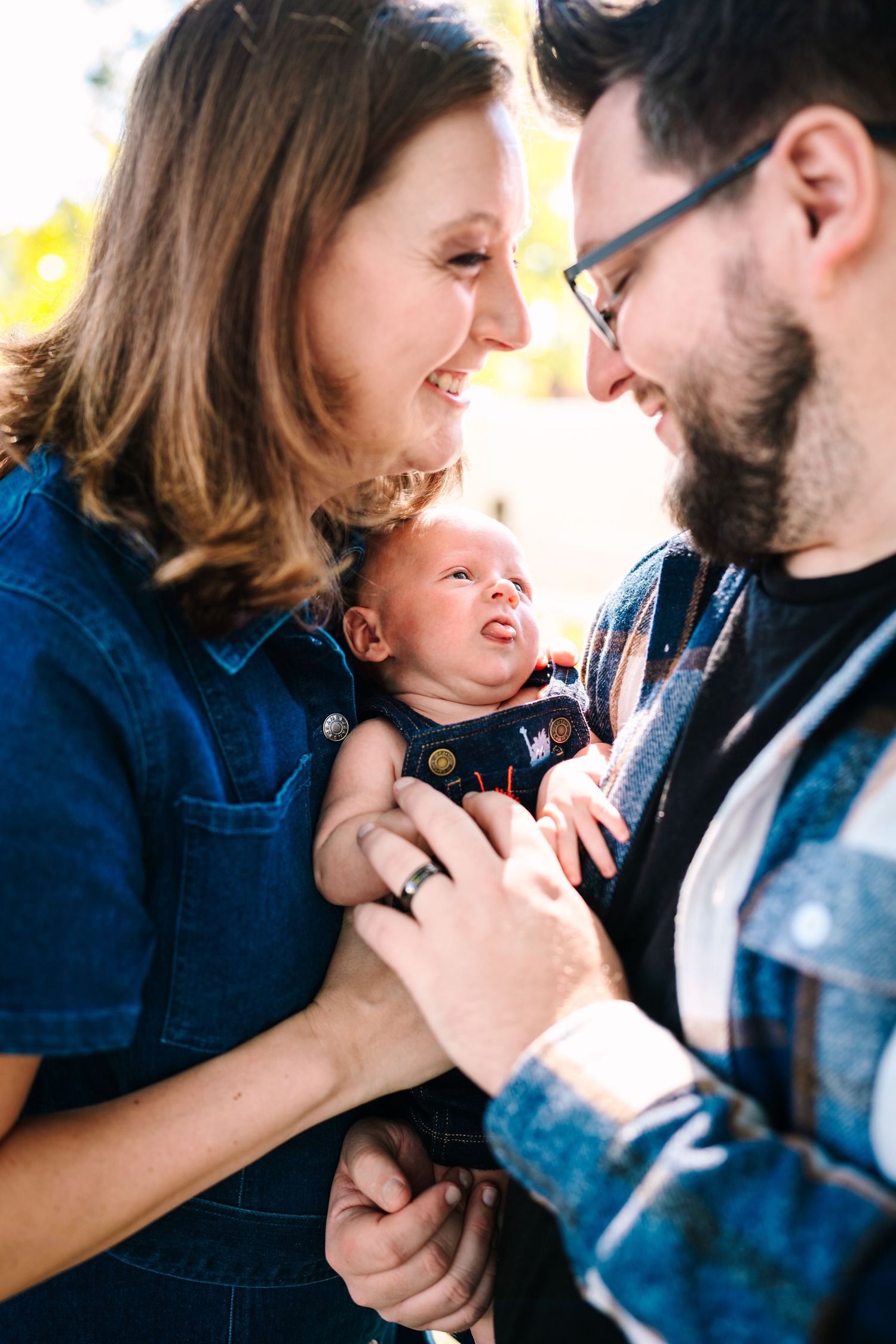 Happy parents smiling at their newborn baby outdoors in warm autumn light.