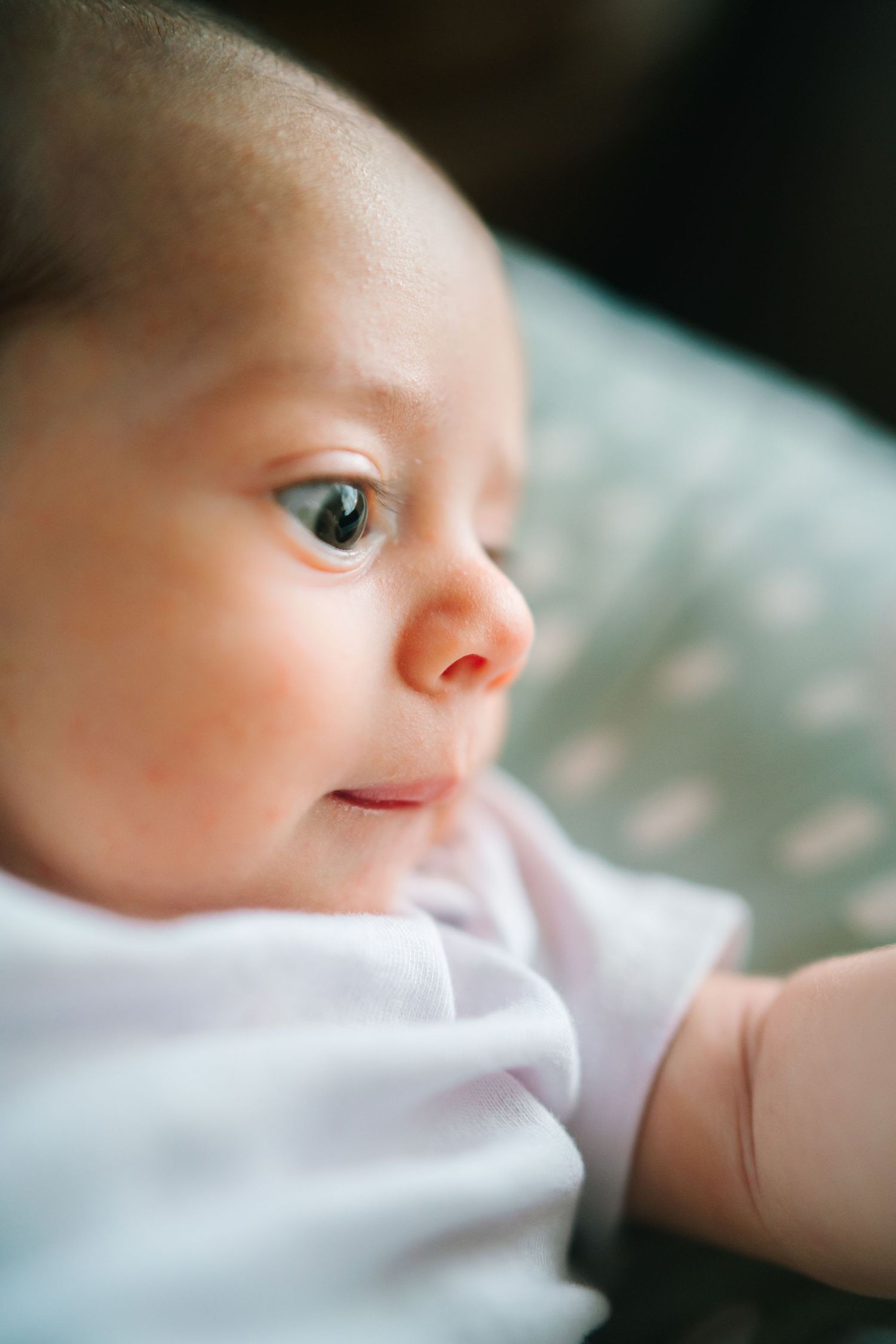 Close-up portrait of an alert newborn baby in pink outfit gazing upward with a gentle smile.