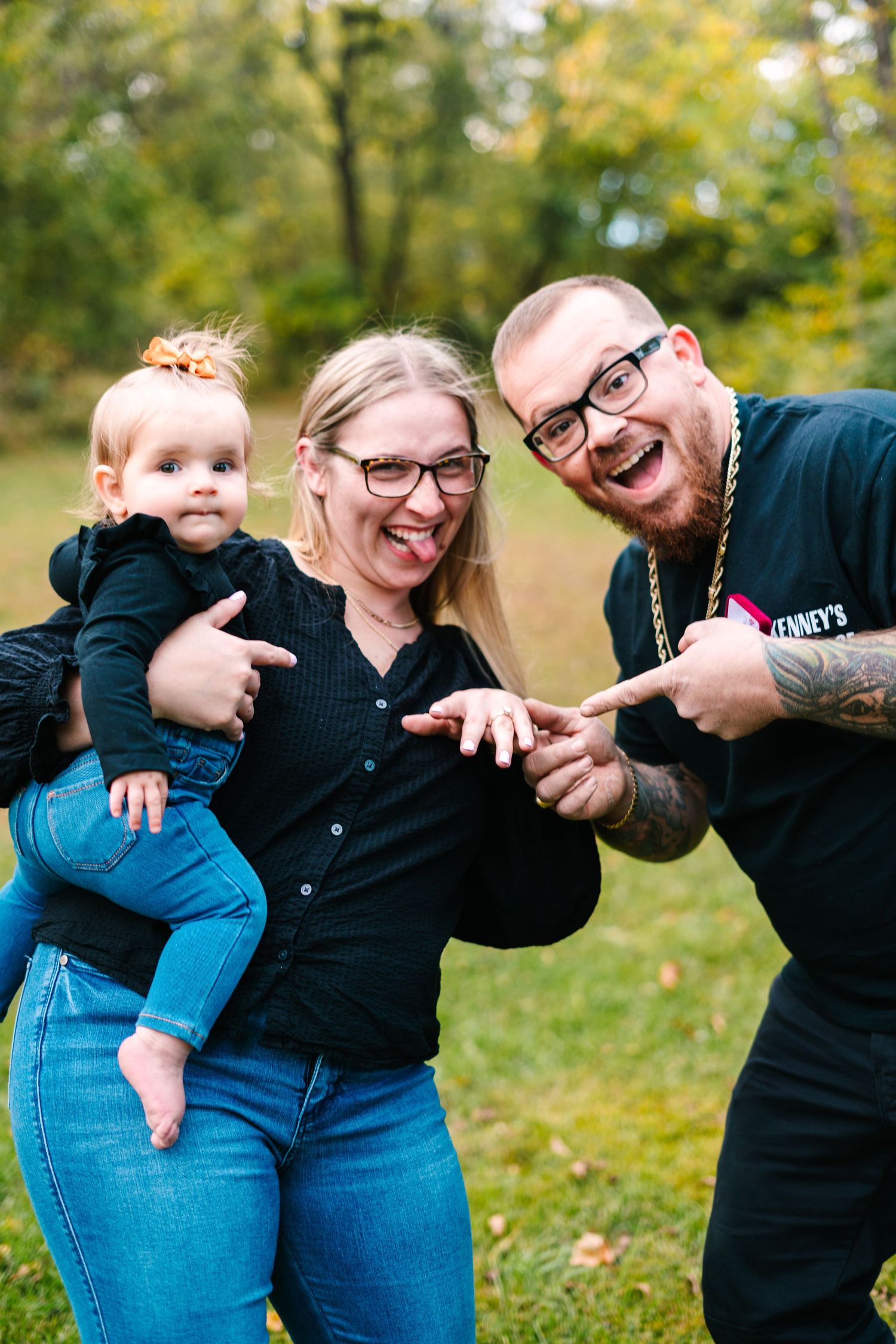 philadelphia wedding photography A laughing couple pointing at a baby girl in a black outfit during an outdoor fall family photo session.