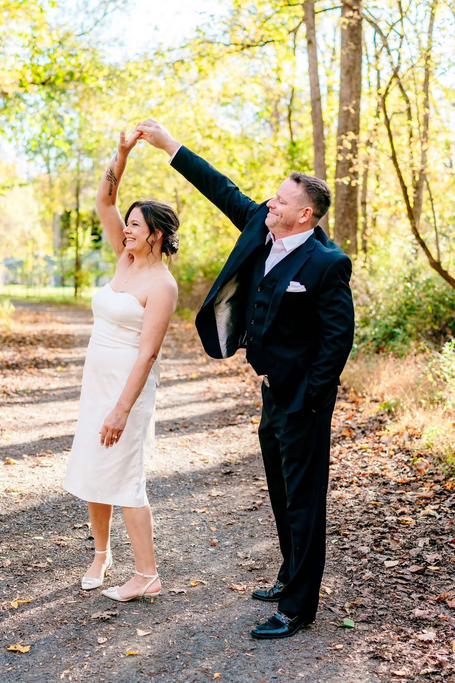 philadelphia wedding photography  Groom twirling bride in white dress on a forest path during an outdoor fall wedding photo session.