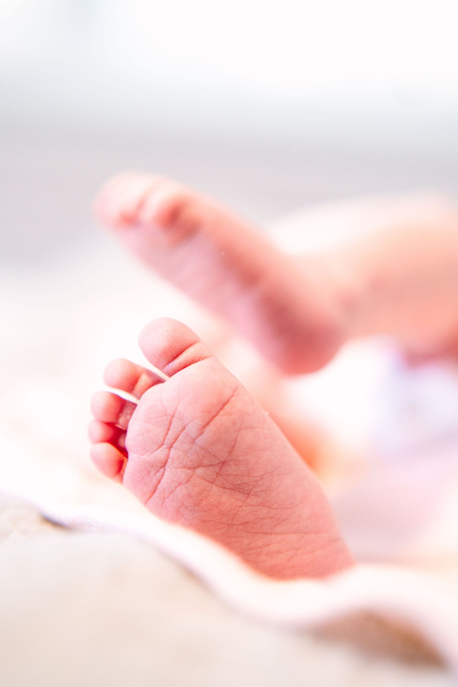 Close-up of tiny newborn baby feet resting on a soft pink blanket, with delicate toes and wrinkled skin.