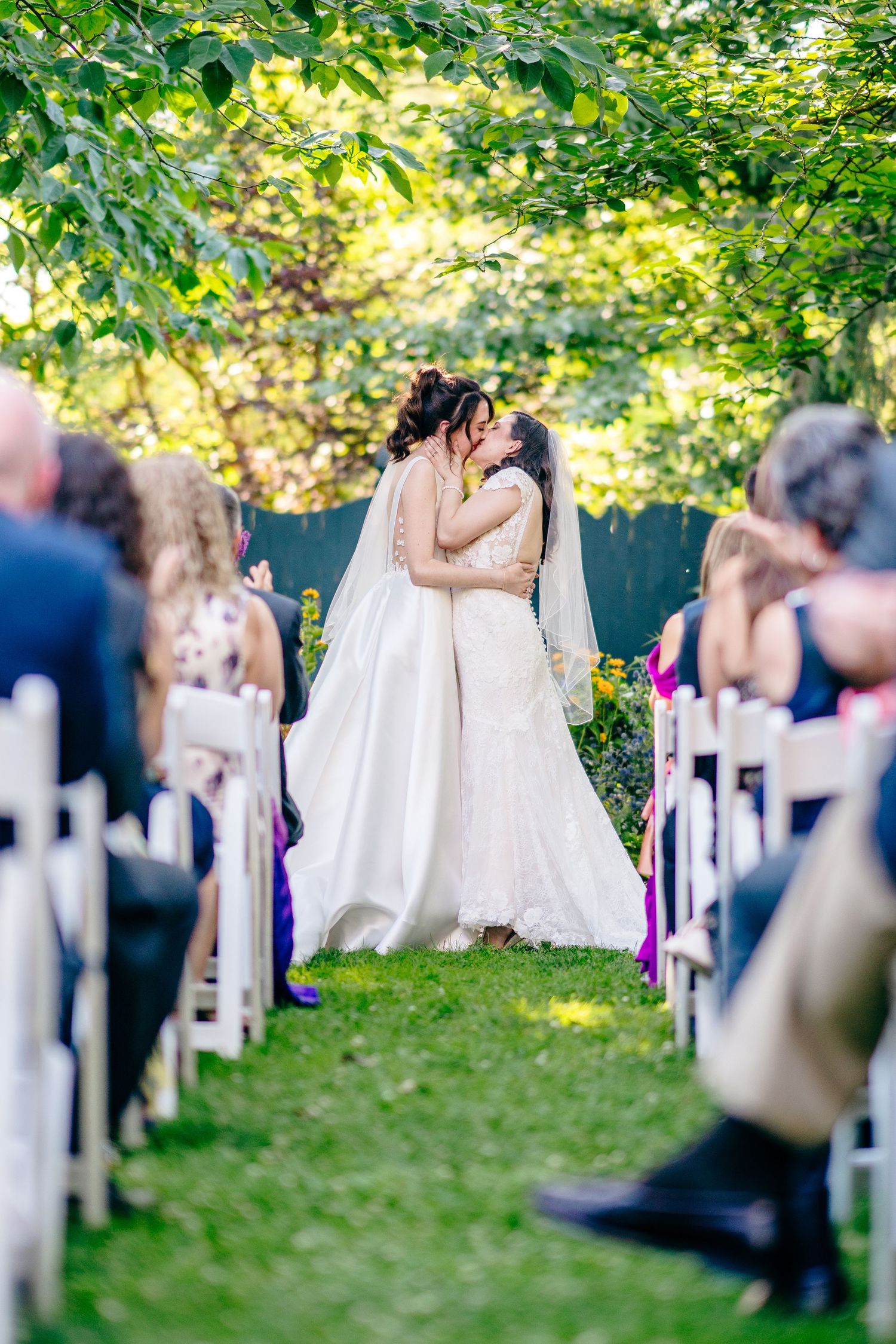 brides share their first kiss at an outdoor wedding ceremony, surrounded by guests seated in white chairsFernbrook farms Philly wedding