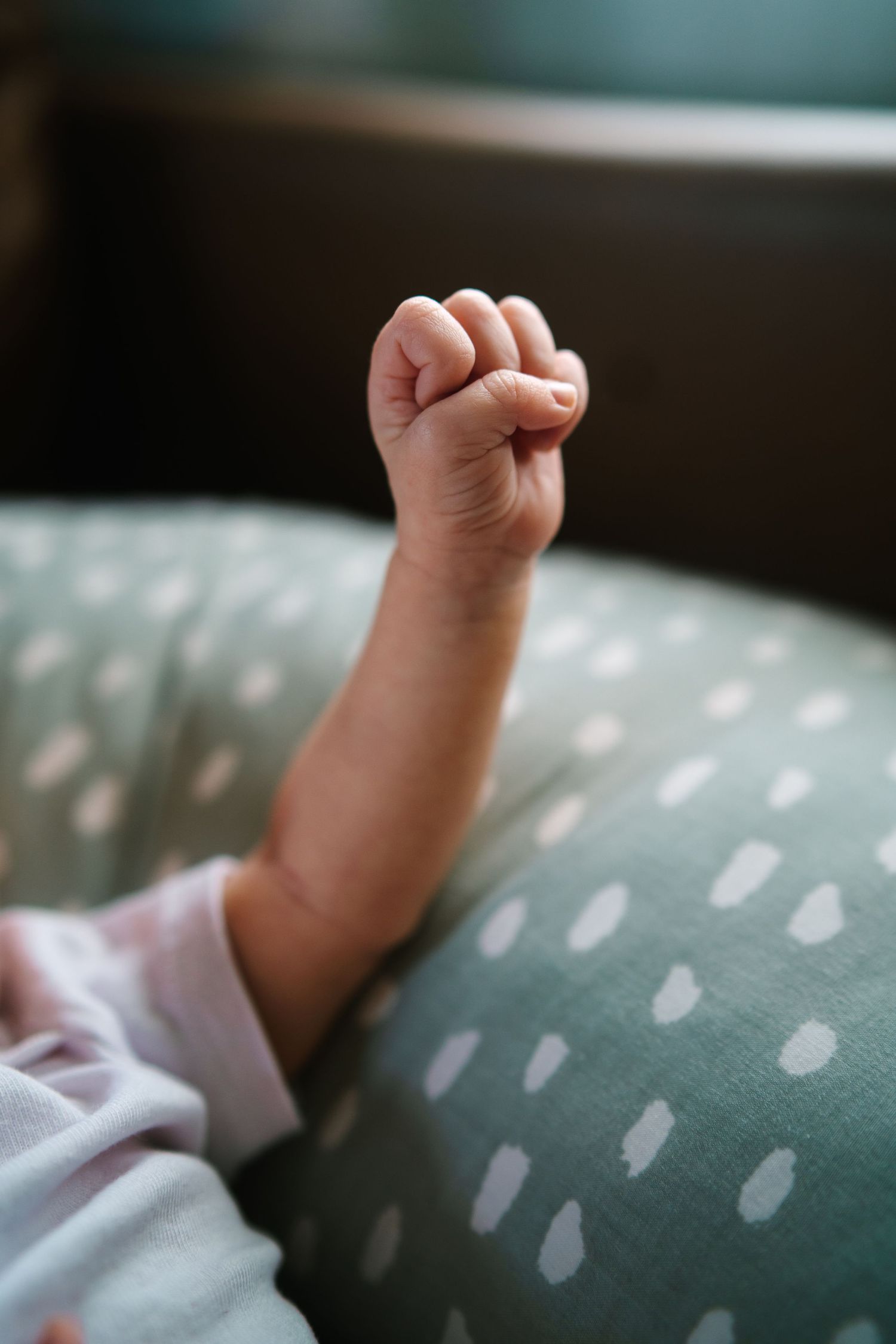 Close-up of a newborn baby's tiny clenched fist raised up while resting on a soft spotted blanket.