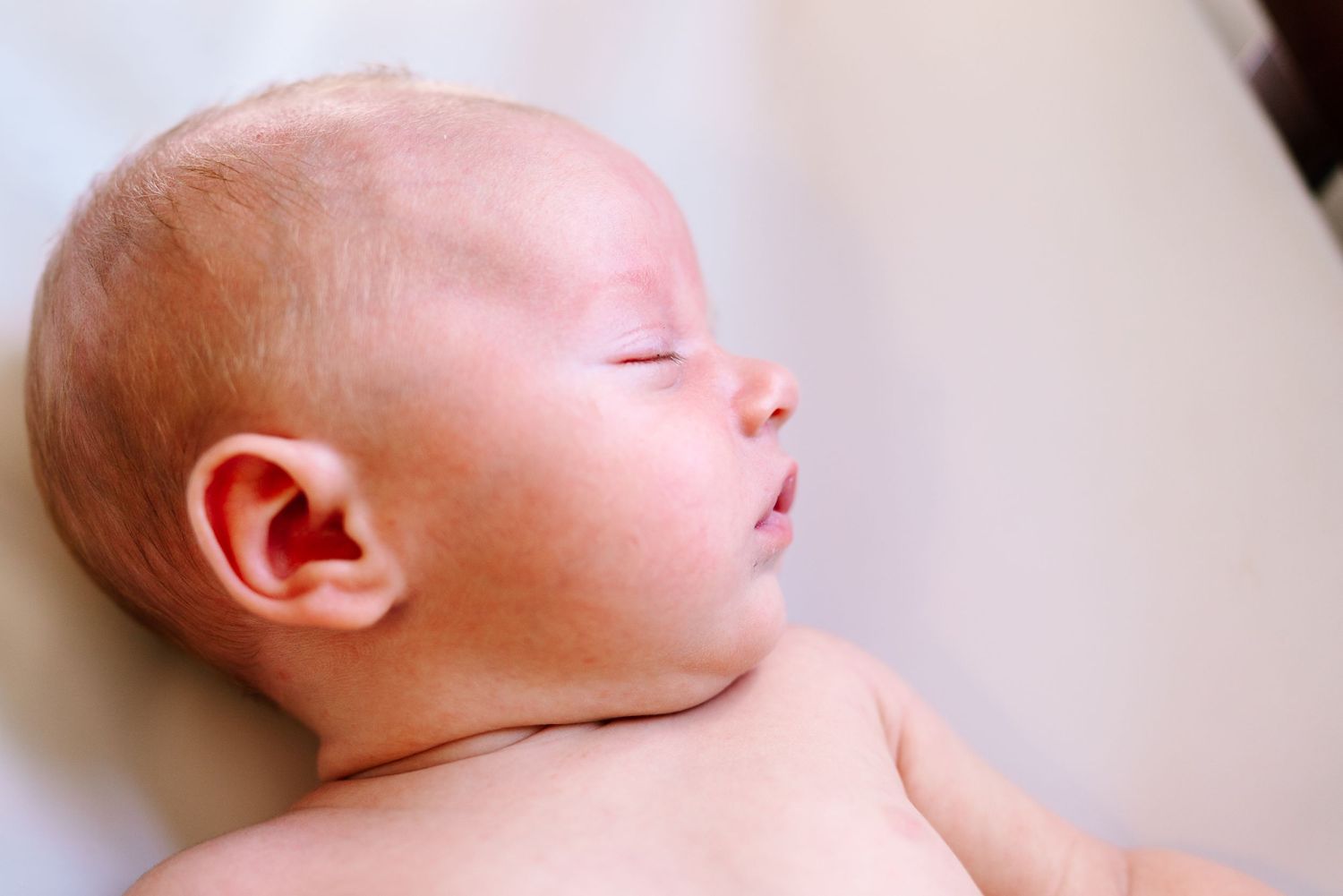 Peaceful newborn baby sleeping with eyes closed, soft skin and delicate features in a serene close-up portrait.