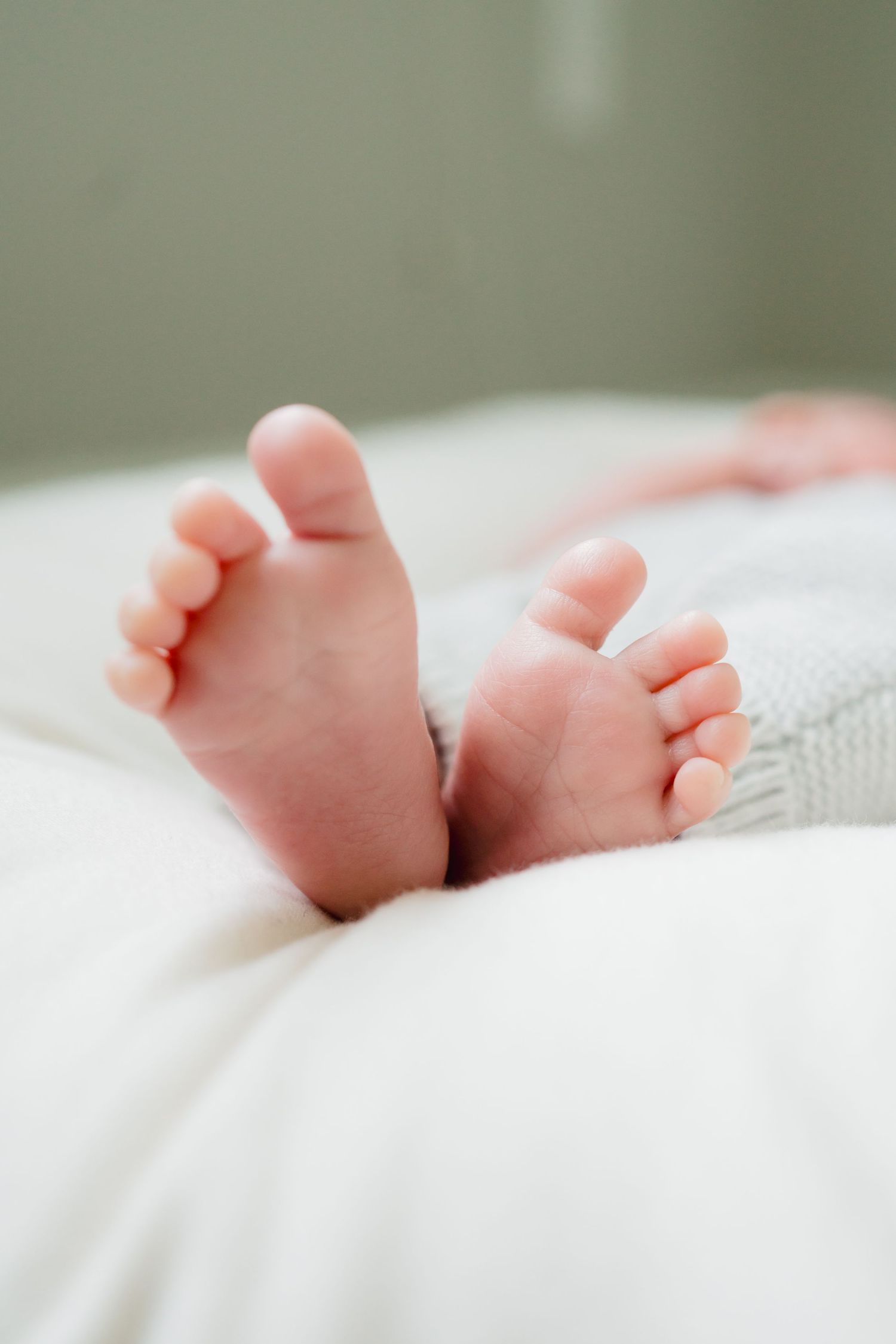 Close-up of tiny newborn baby feet peeking out from a soft white blanket on a bed.
