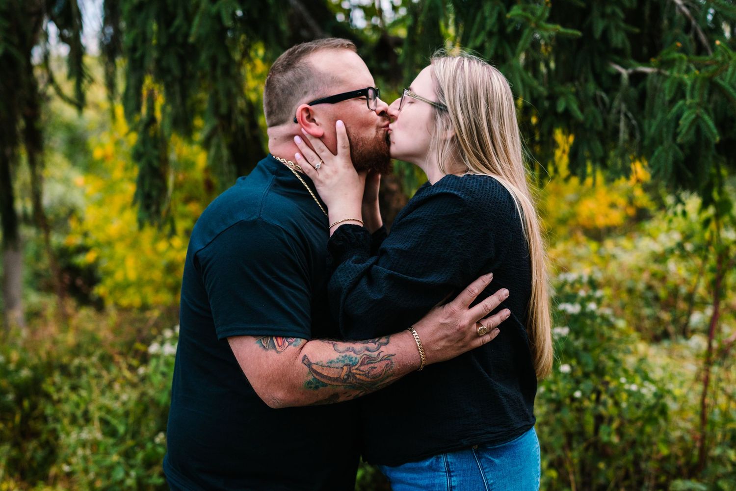 philadelphia wedding photographer A couple shares a romantic kiss outdoors surrounded by lush green and yellow foliage in a garden setting.