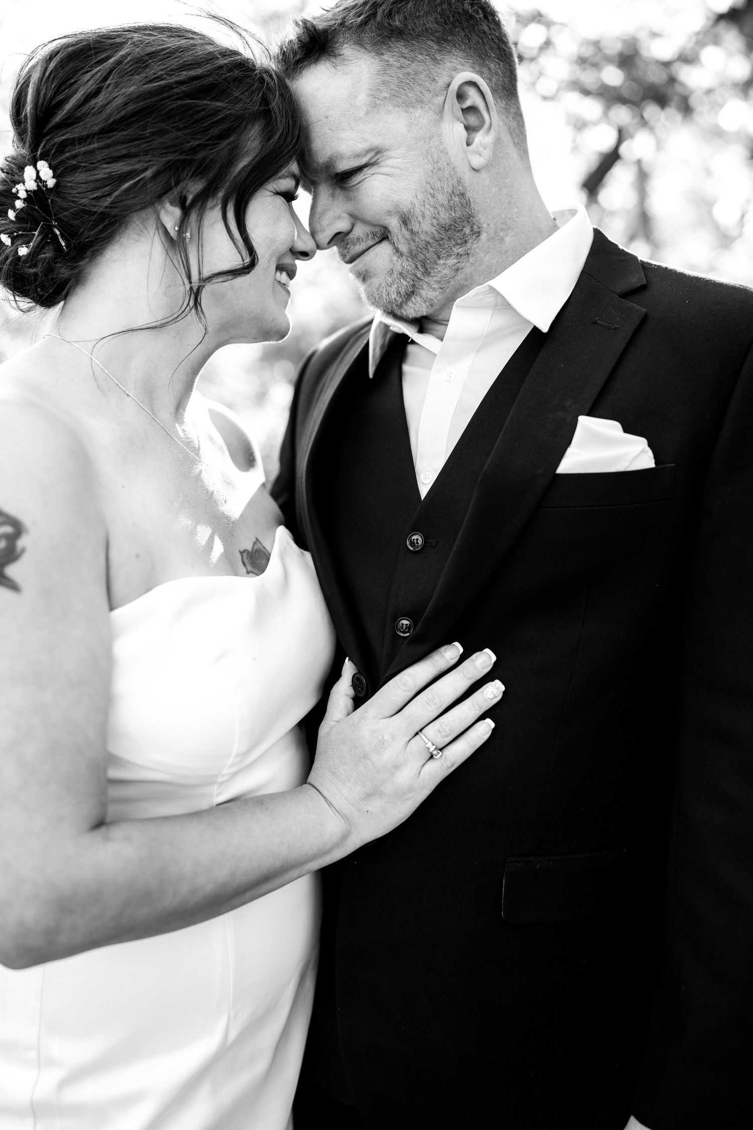 Black and white photo of a smiling bride and groom in wedding attire sharing an intimate moment, touching foreheads tenderly.