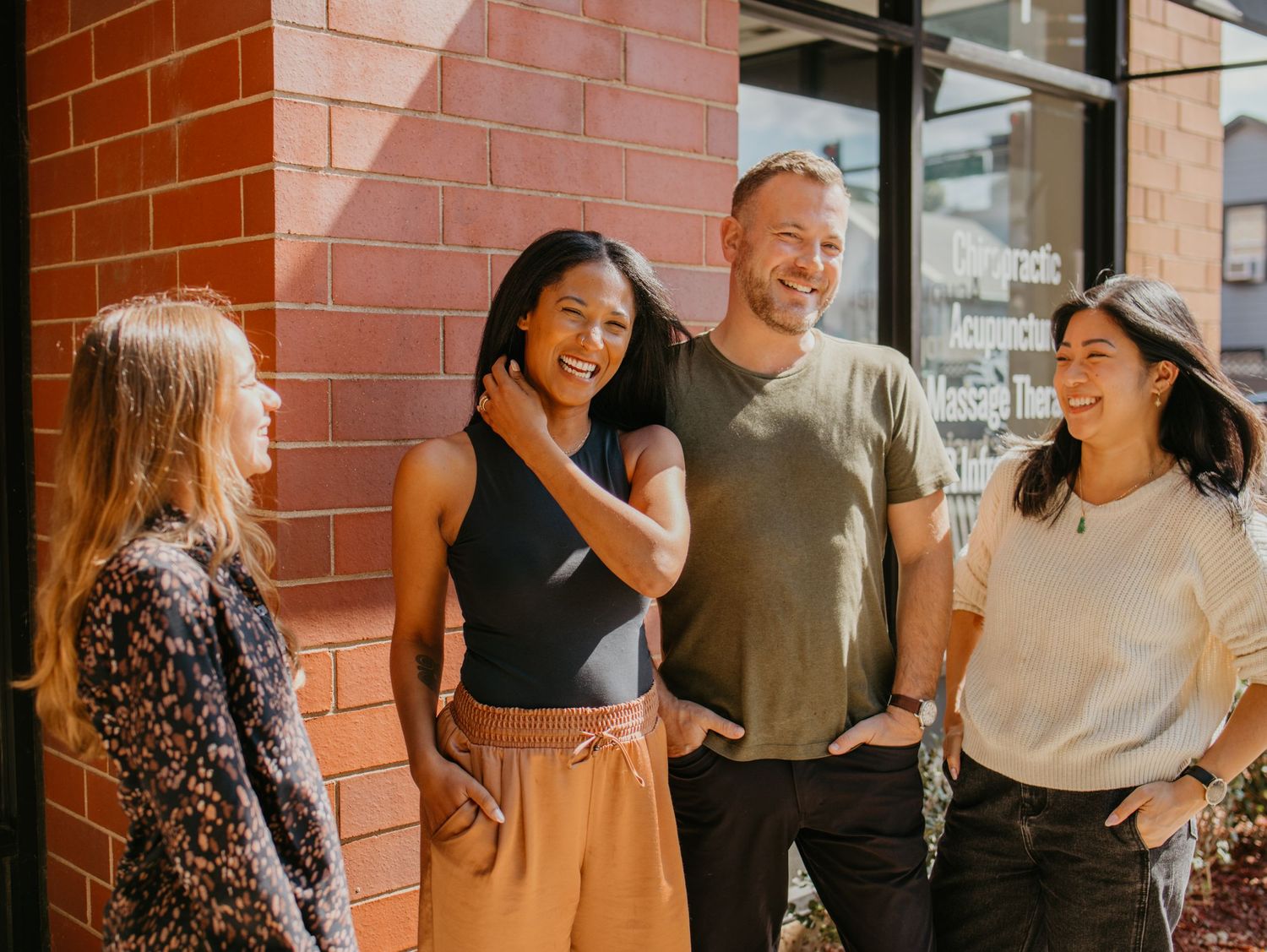 Group of friends laughing and chatting together against brick wall backdrop.