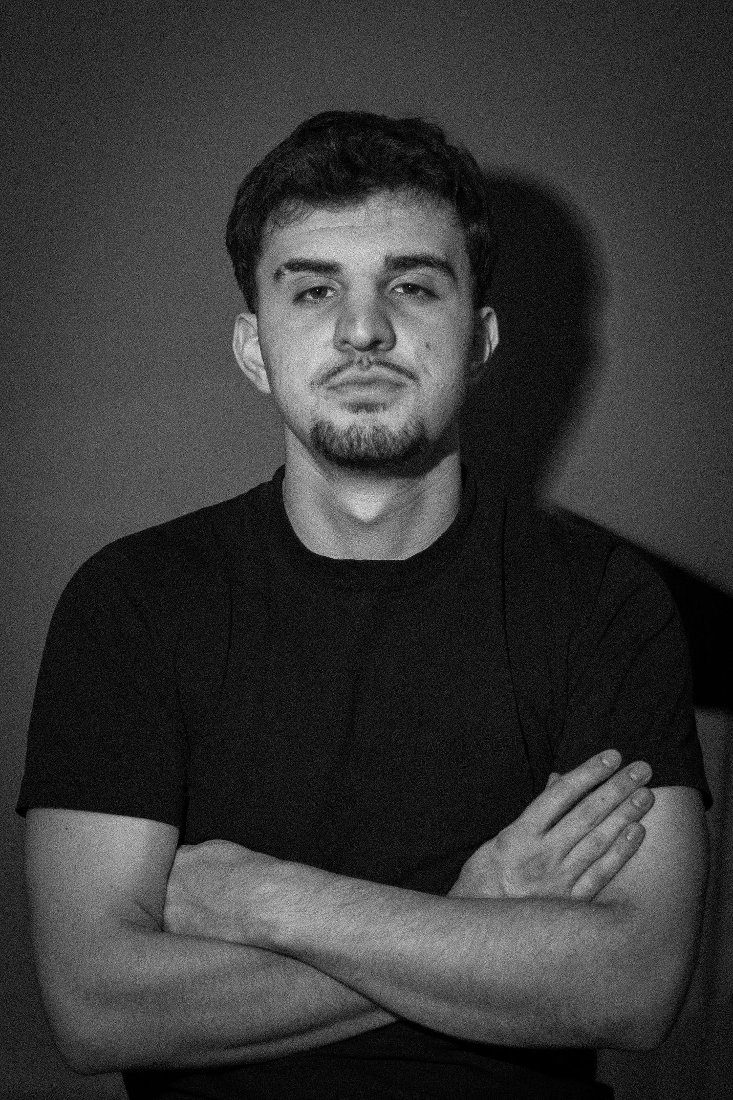 Young man in black t-shirt posing with arms crossed in black and white portrait.