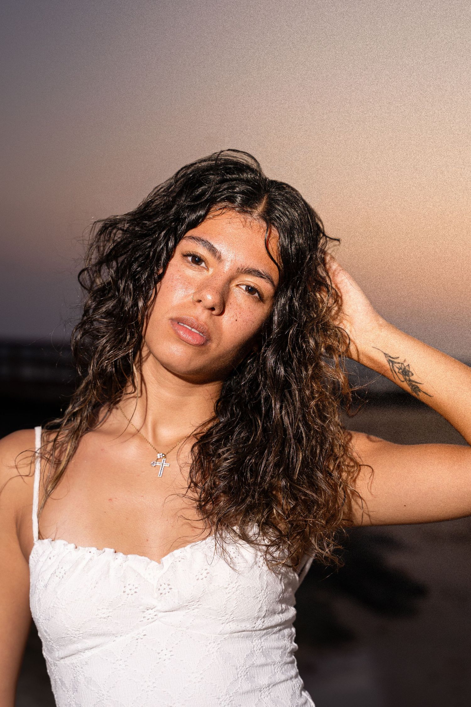 Young woman with curly hair in a white dress posing at sunset on the beach.

portrait