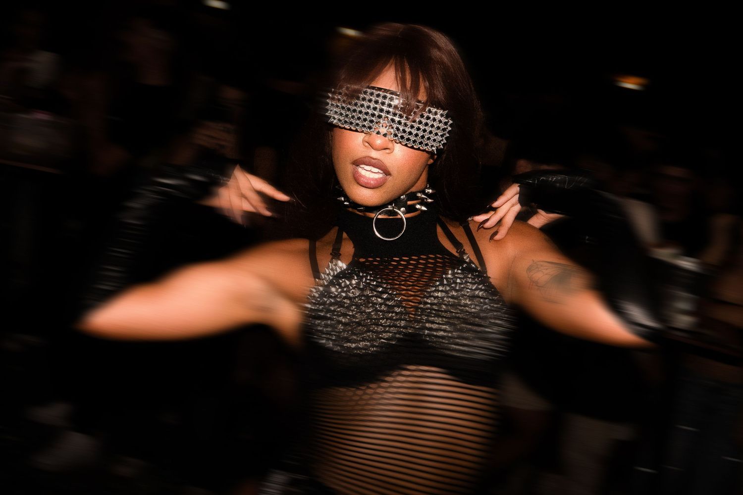 Woman dancing in rhinestone blindfold and mesh outfit at a dark nightclub event.

event